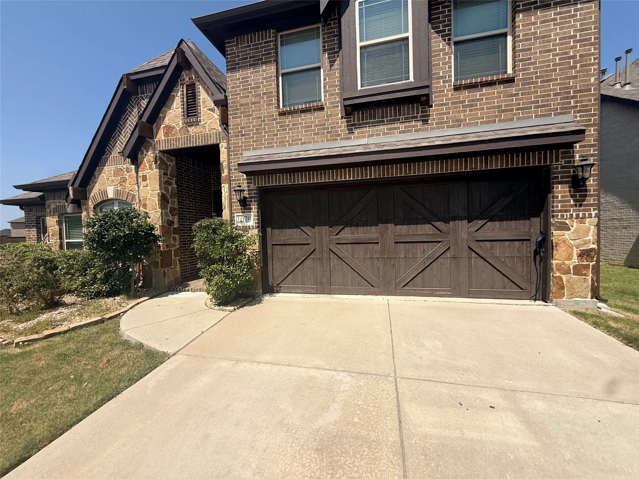Brick and stone facade featuring a wood-finish garage door, exterior lighting, and a concrete driveway