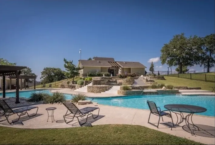 Resort-style pool with integrated waterfall features, extensive concrete decking, and layered stone retaining walls