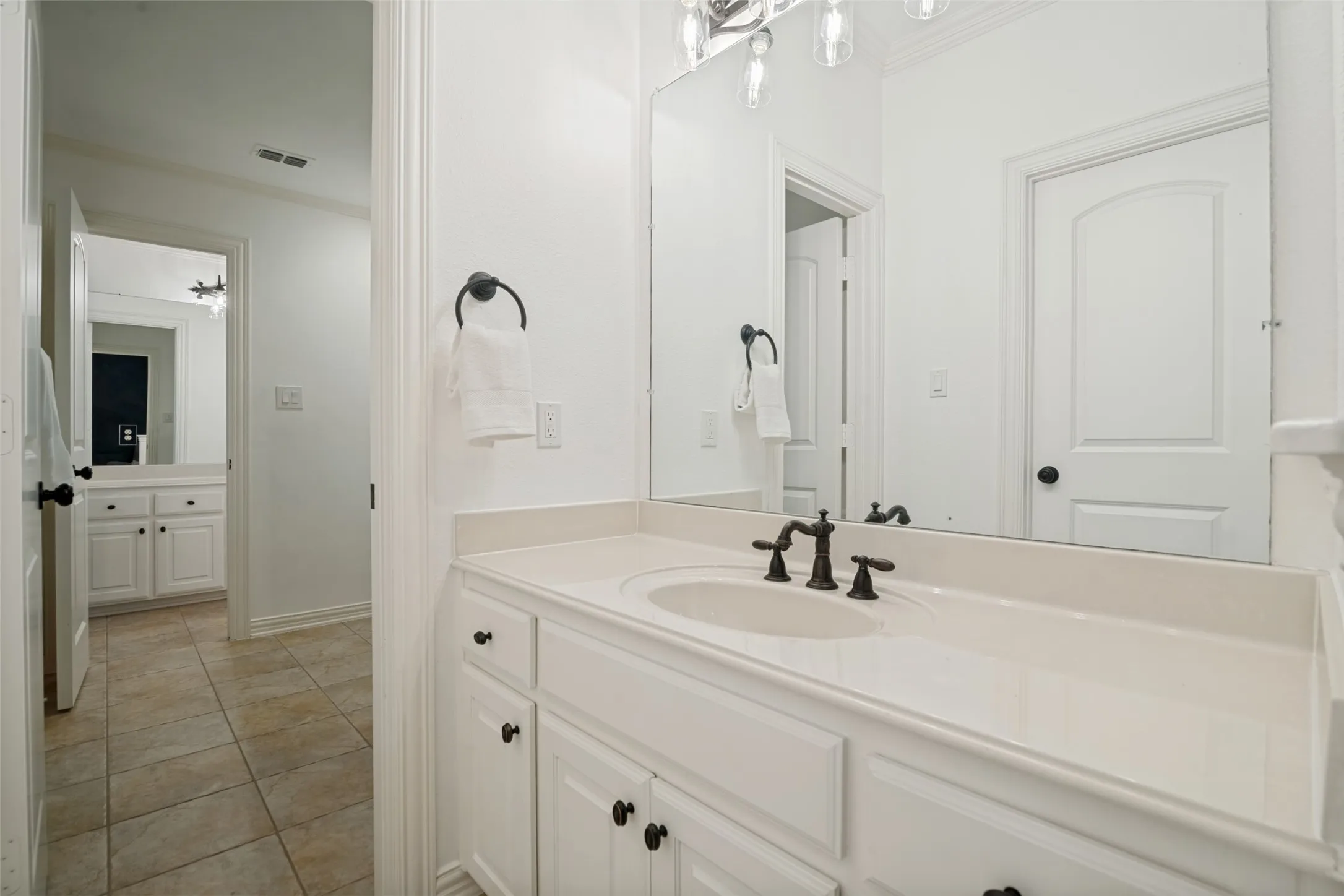 Jack and Jill bathroom vanity with an integrated sink, white cabinetry, a large wall mirror, and a bronze-finish faucet