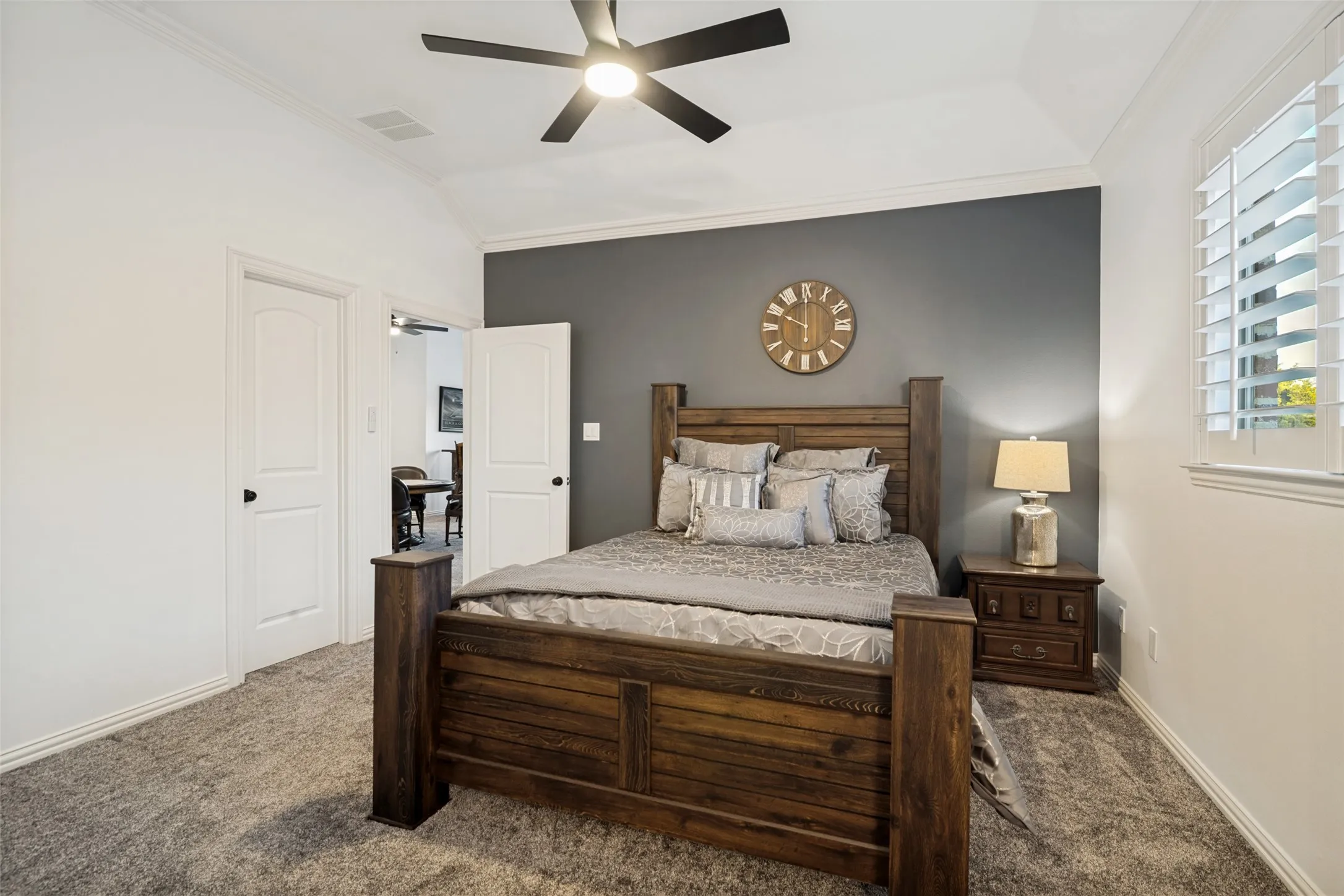 Vaulted ceiling with crown molding, ceiling fan, white paneled doors, textured carpet, and plantation shutters