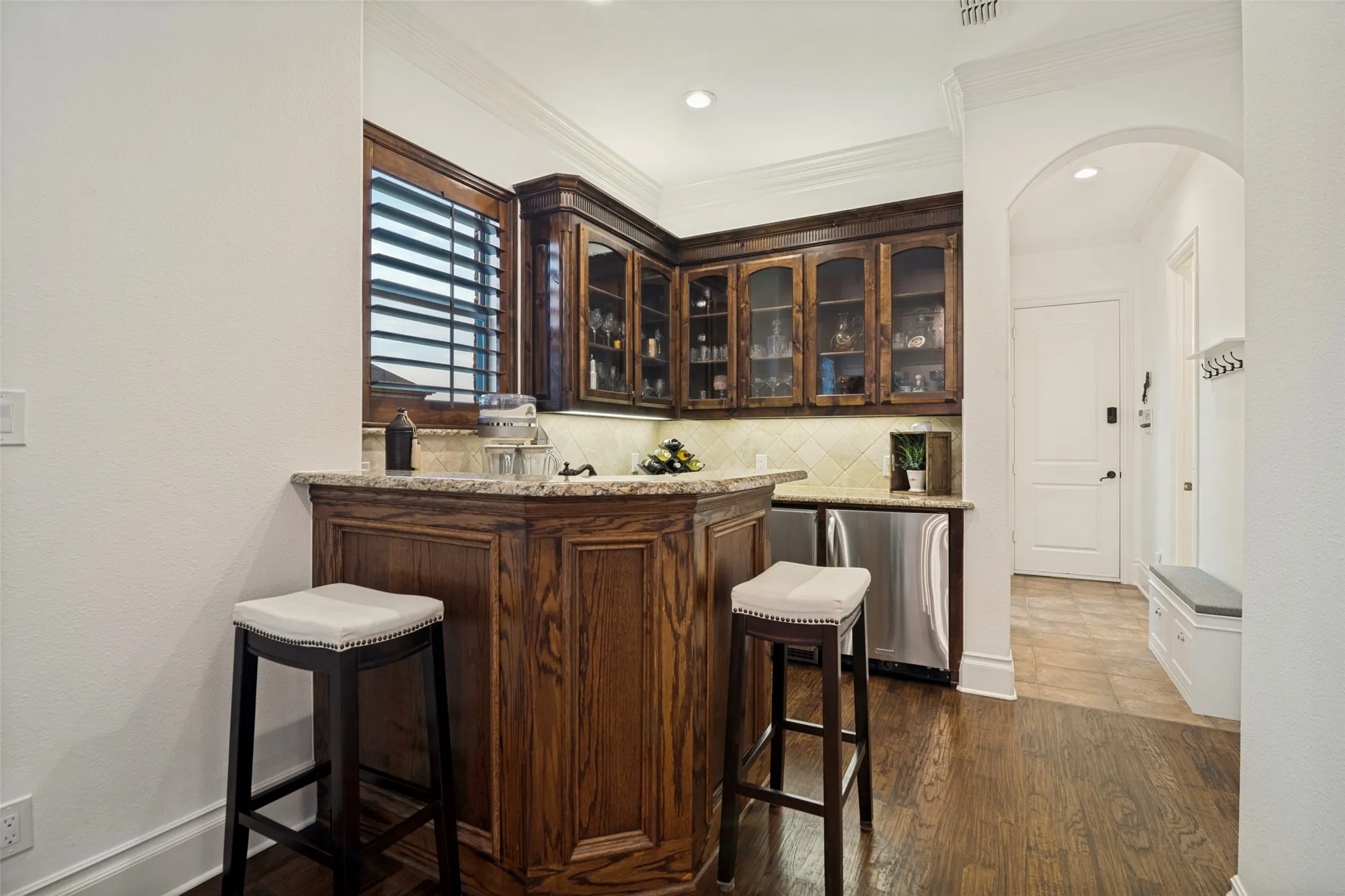Wet bar with custom wood cabinetry, glass fronts, under-cabinet lighting, stainless steel appliances, and a sink and granite countertop