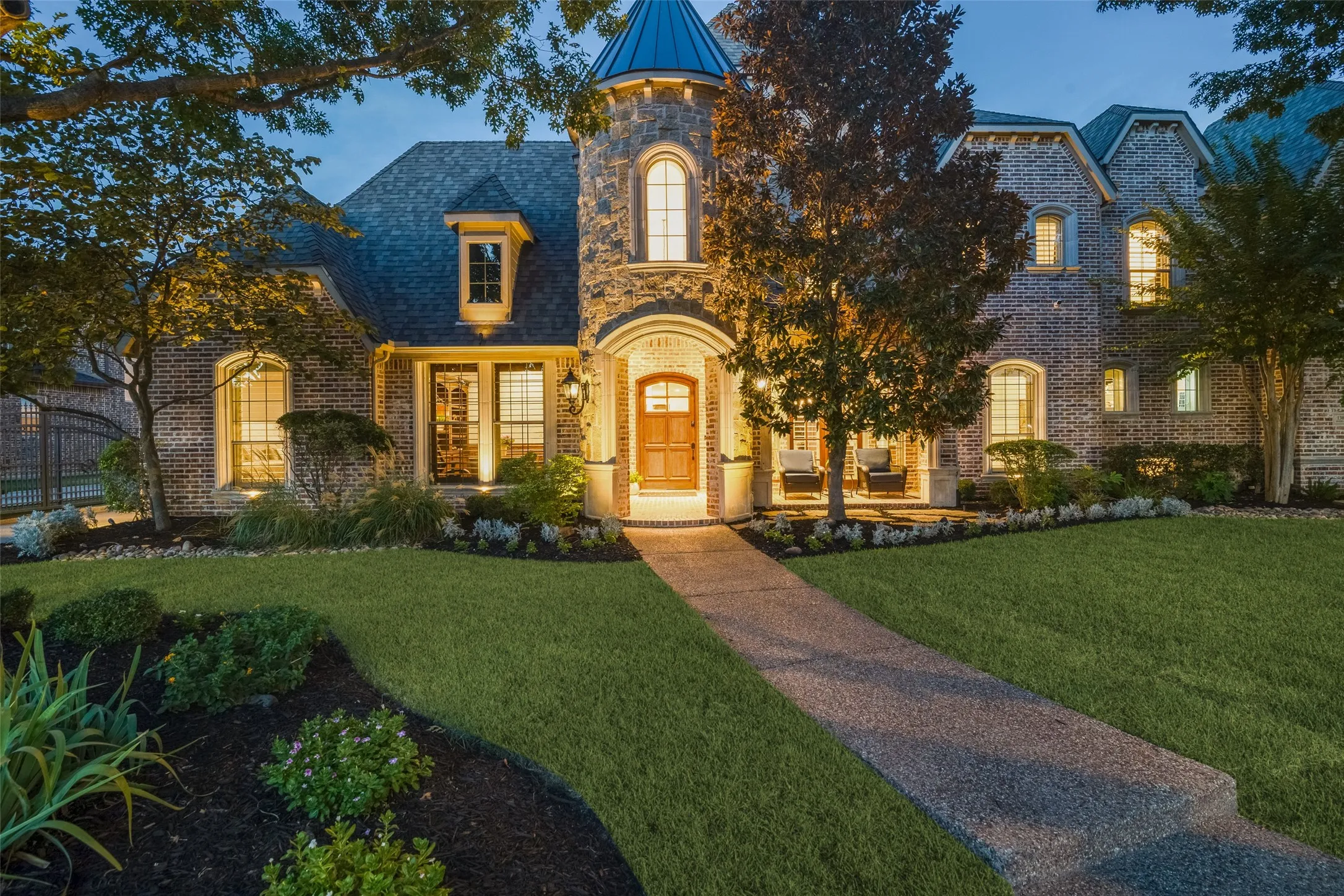Brick and stone exterior with a turret feature, arched entry, multiple windows, and a landscaped front yard with a concrete walkway