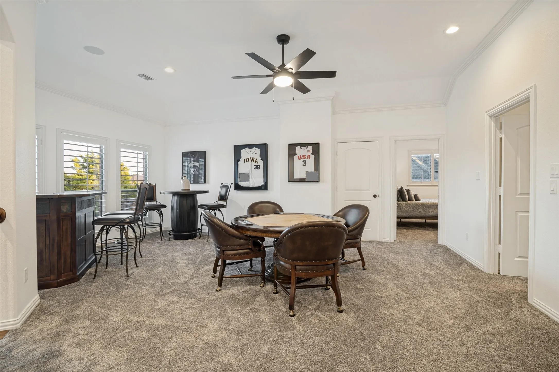 Spacious room featuring neutral carpeting, white walls, multiple windows with louvered shutters, and a ceiling fan with integrated lighting