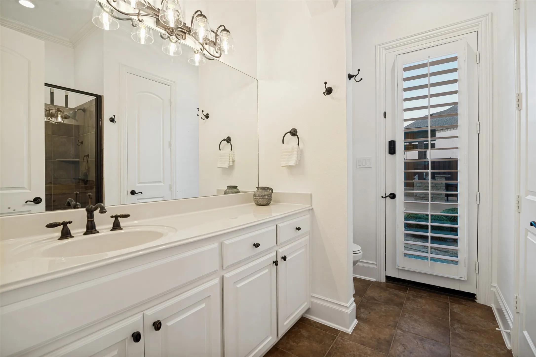 Bathroom with door leading to backyard pool area. White vanity with an integrated sink and bronze-finish faucet
