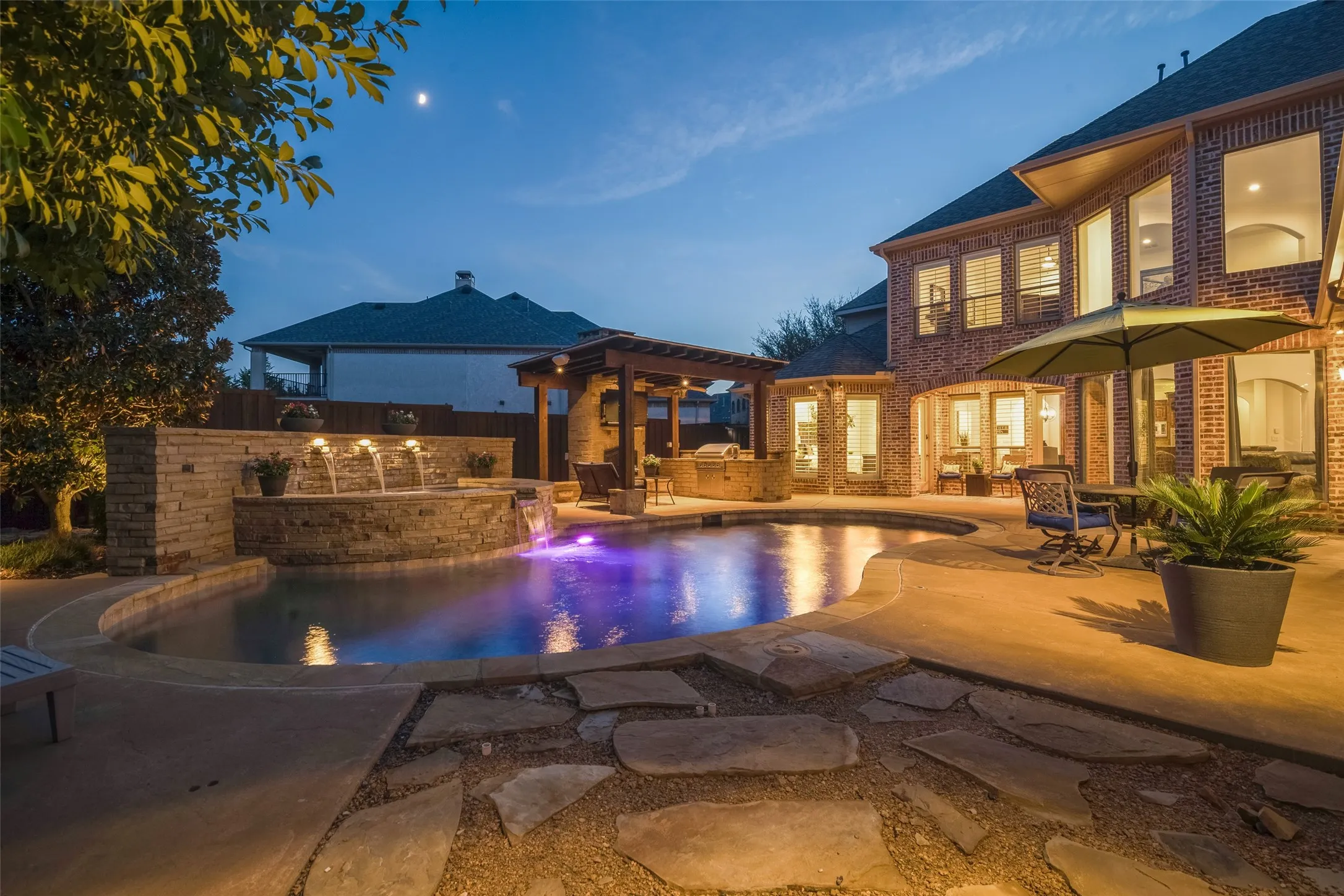 Brick exterior featuring multiple windows, a curved swimming pool, stone water features, and an outdoor pergola with built-in cabinetry