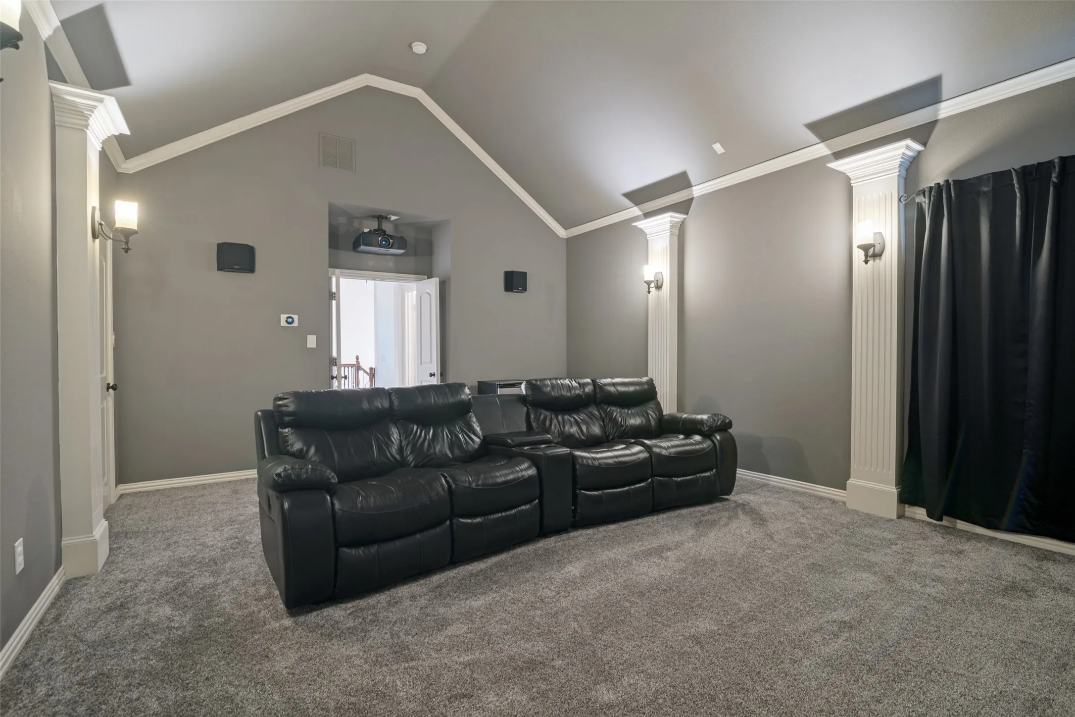 Vaulted ceiling with crown molding, wall-mounted sconces, and built-in architectural columns