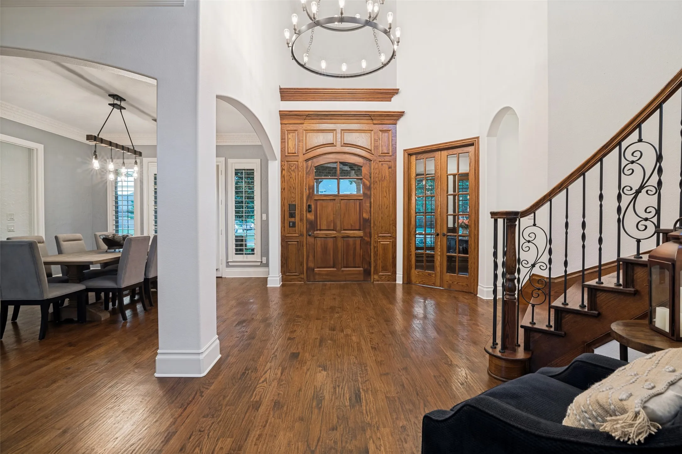 Hardwood flooring, arched doorways, decorative wrought iron staircase, high ceilings, and a substantial wood entry door with transom