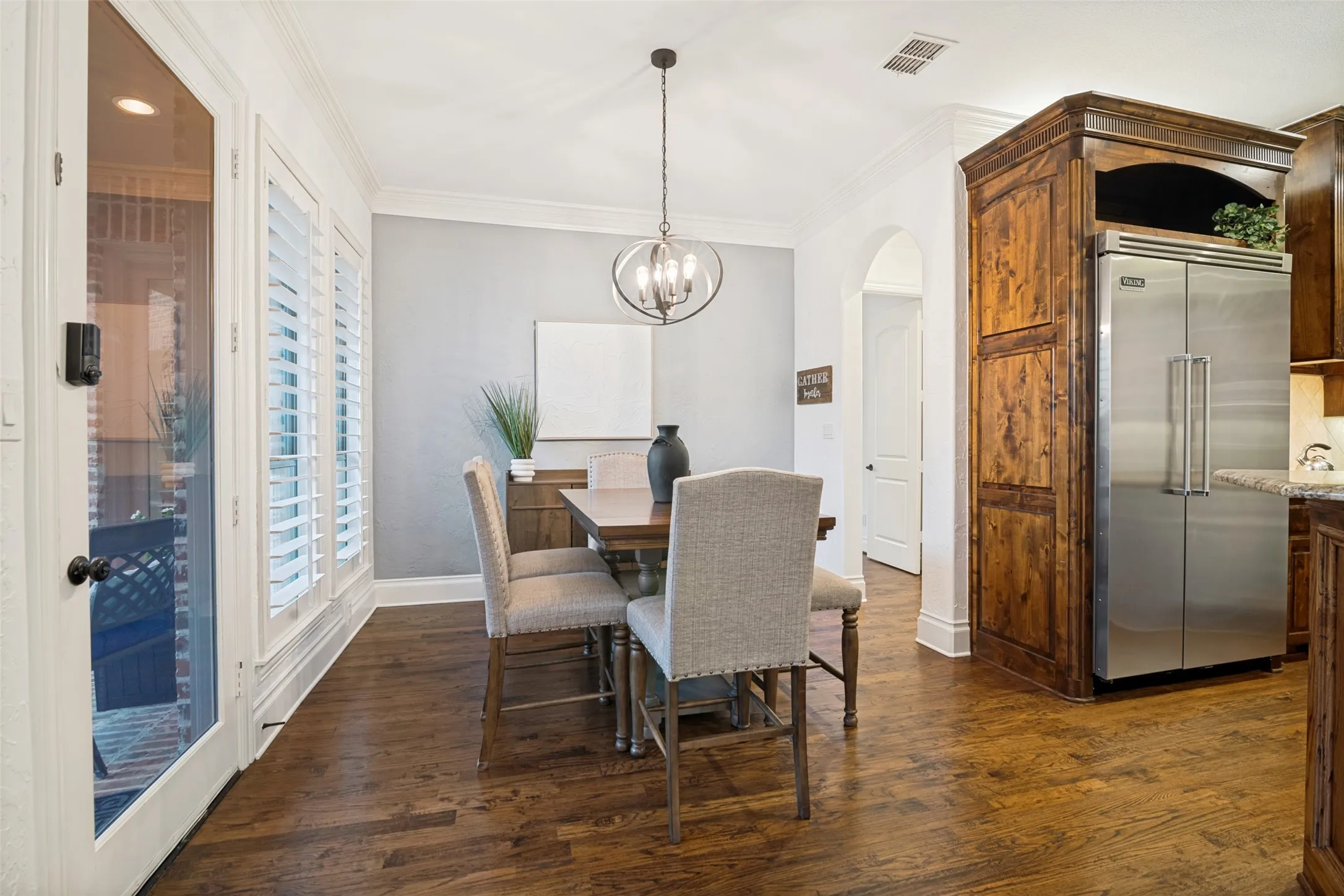Hardwood-finish flooring, built-in wooden cabinetry, plantation shutters, stainless steel refrigerator, and an arched entryway