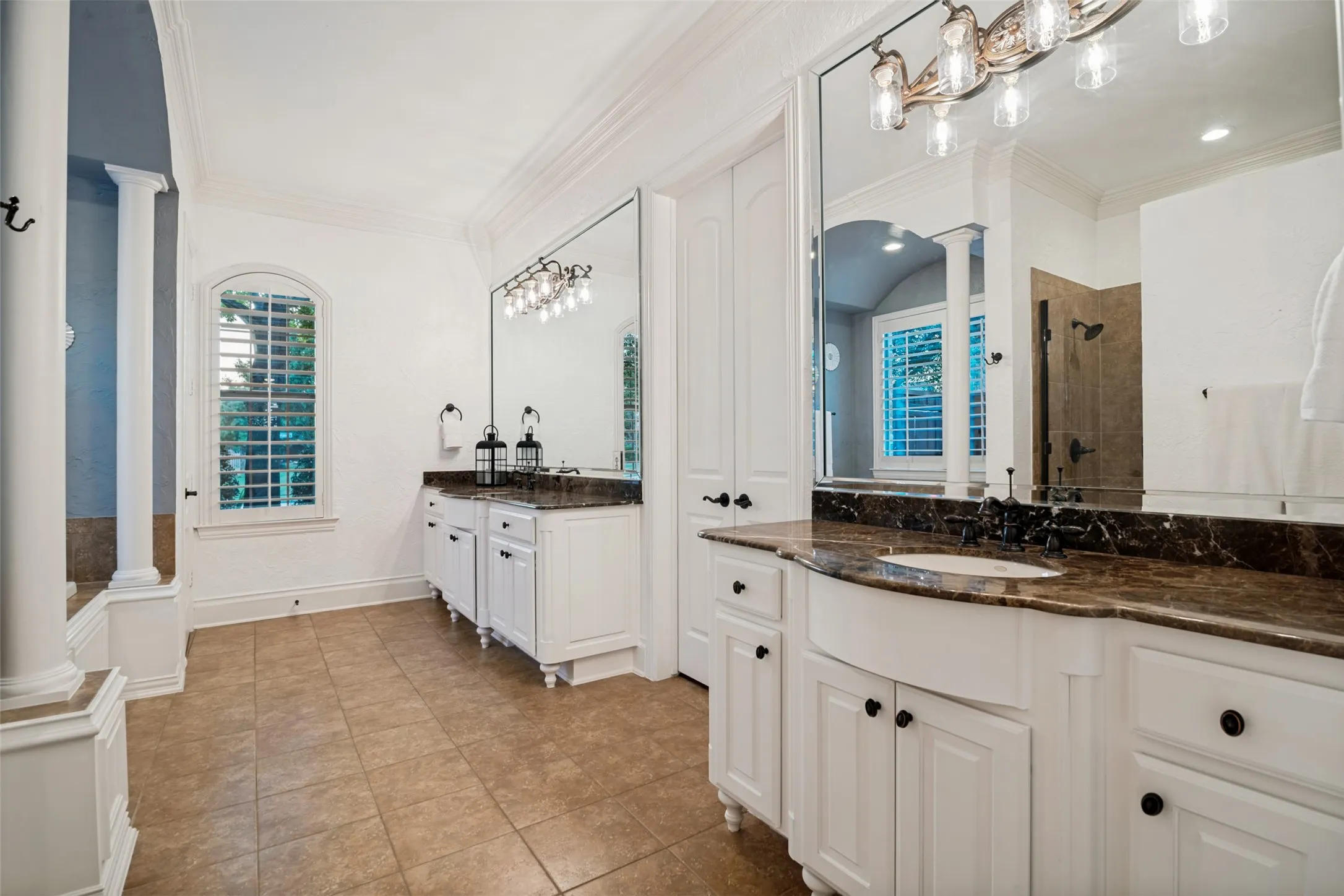 Dual vanities with stone countertops, a large framed mirror, white cabinetry, and a window with plantation shutters