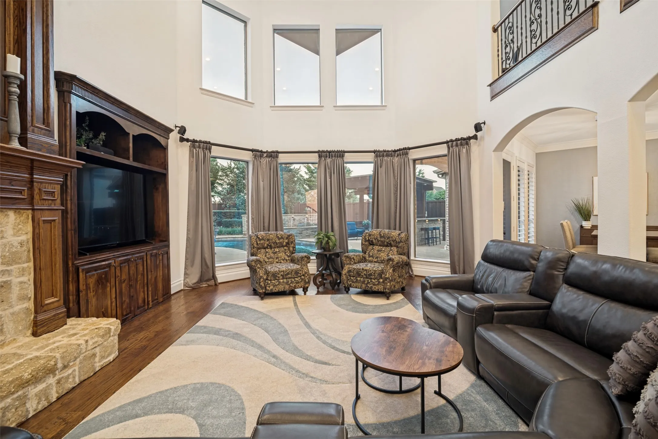 Two-story living area with high ceilings, wood-finish flooring, and a stone-clad fireplace