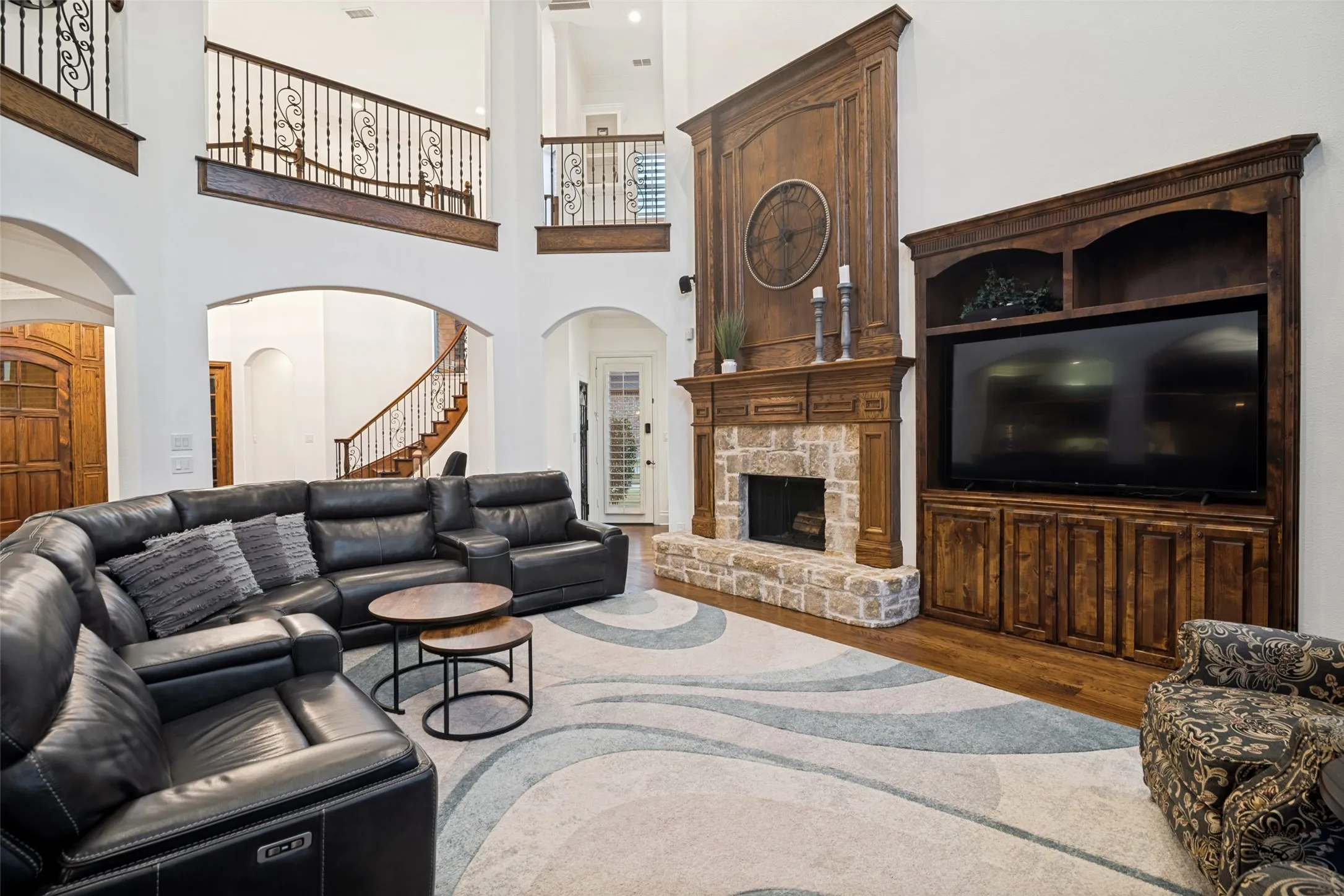 Two-story living area featuring a stone-faced fireplace with a wood-mantel, built-in media cabinetry, and an arched entryway