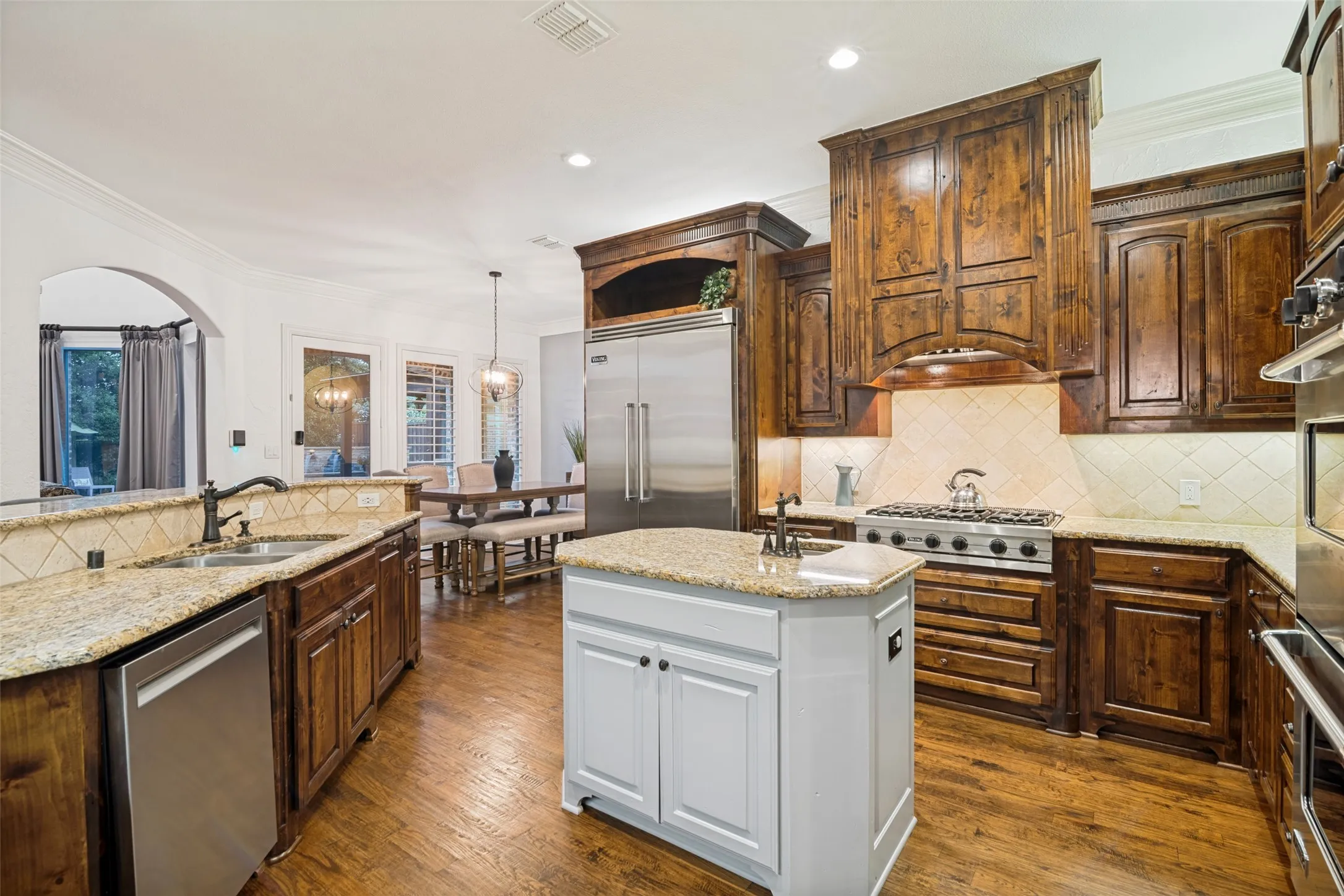 Gourmet kitchen with wood-finish flooring, stainless steel appliances, granite countertops, and custom cabinetry