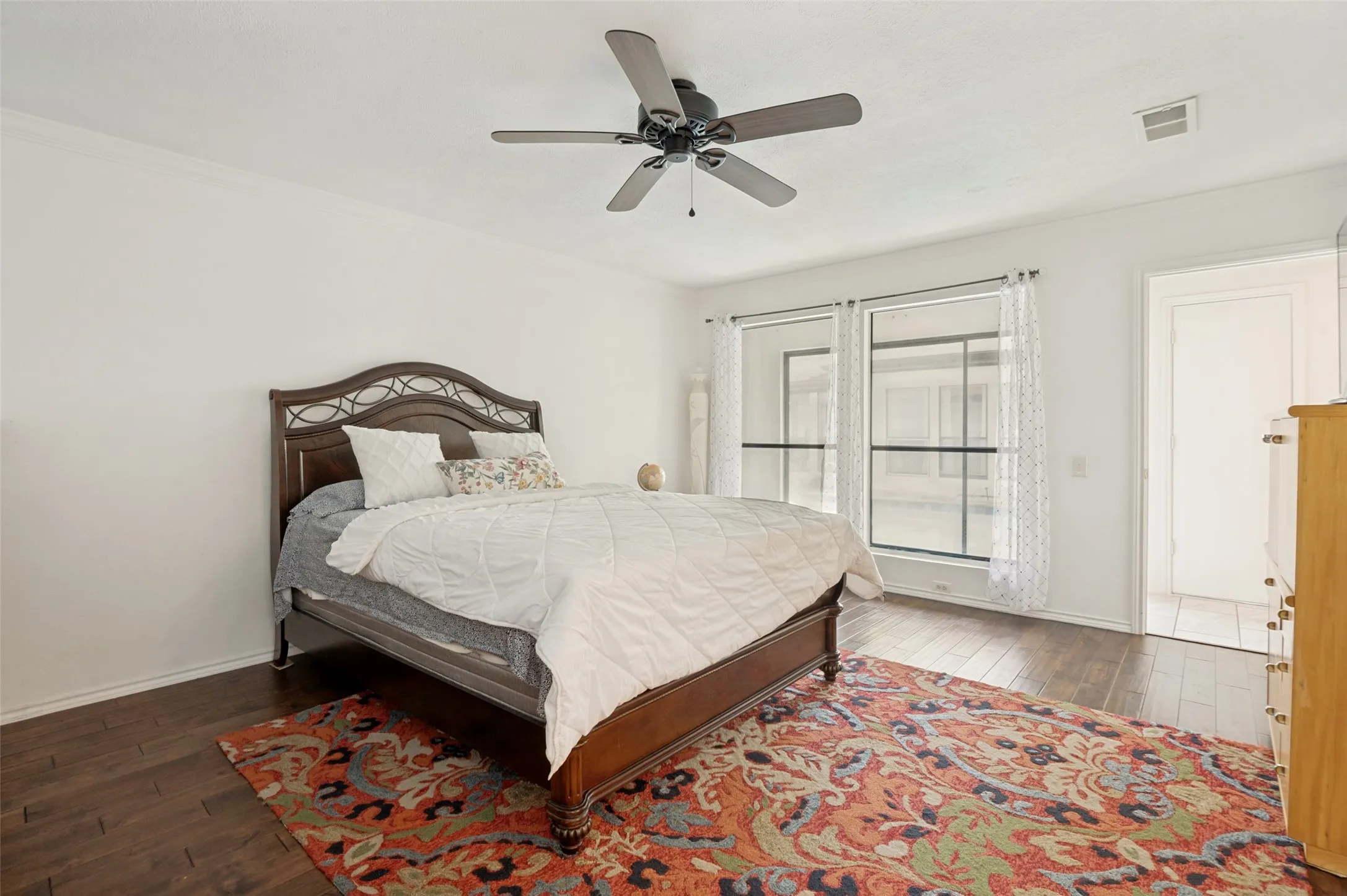 Master bedroom featuring wood-finish flooring with a ceiling fan, dual large windows facing the pool.
