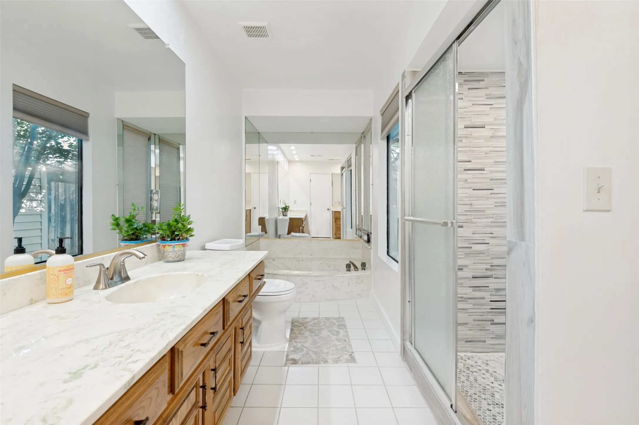 Master bathroom with white tile flooring, a long wood-finish vanity with a light-toned countertop, a built-in shower with a mosaic tile wall, and a large soaking tub