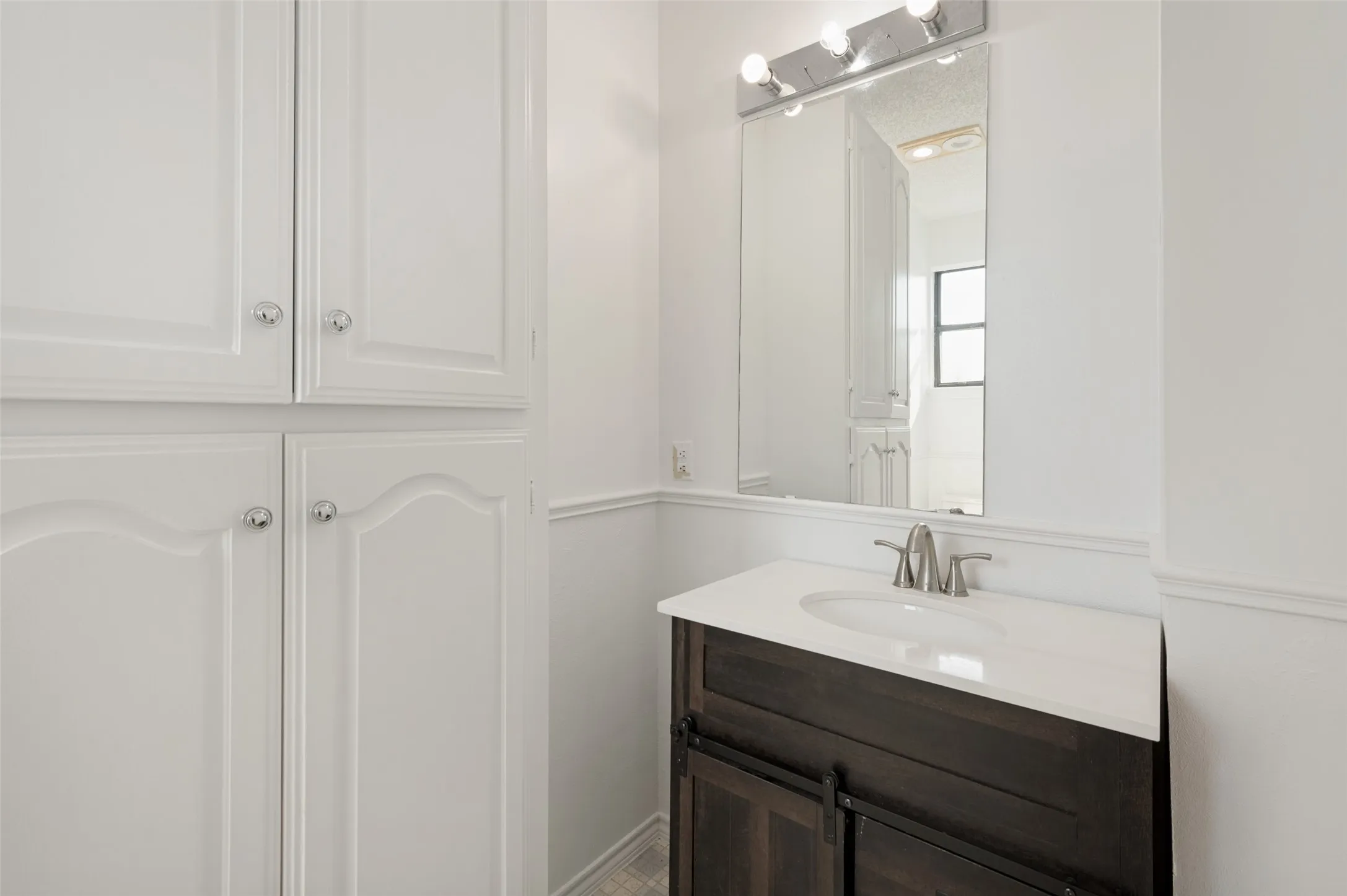 Upstairs bathroom with mounted cabinetry, dark wood-finish vanity with a white countertop, and a rectangular mirror with integrated lighting
