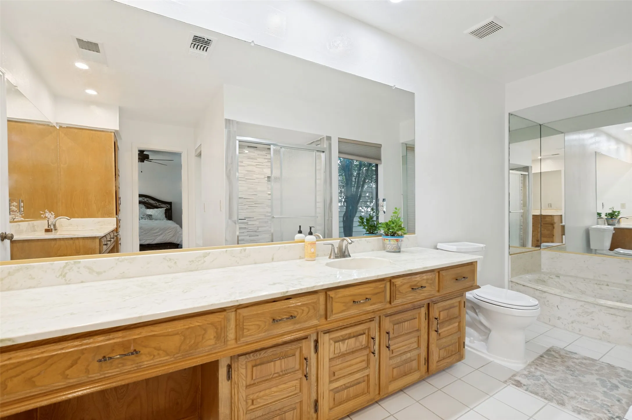 Master bathroom with expansive vanity with wood-finish cabinetry, light-toned countertop, and dual sinks.