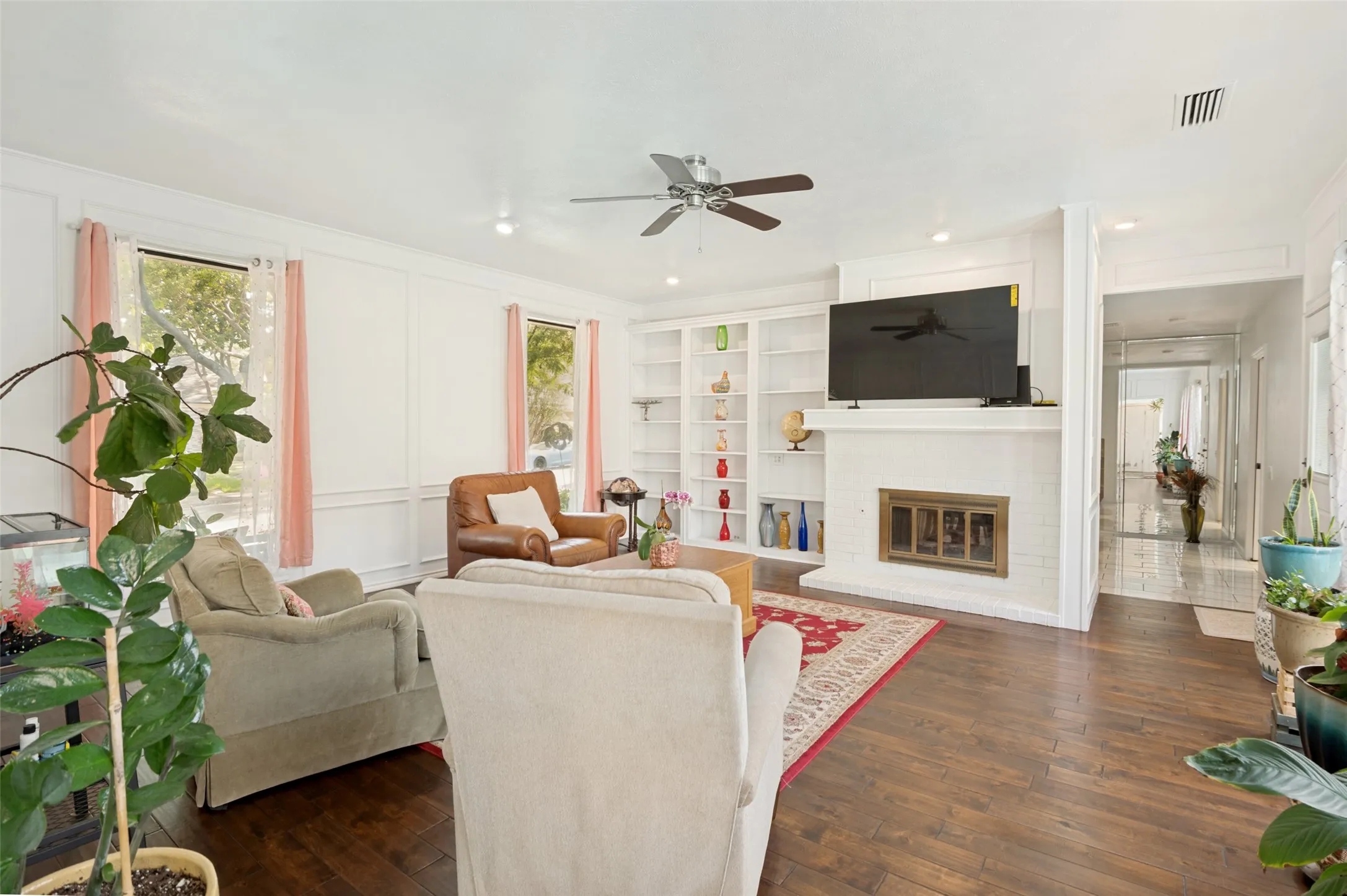 Wood-finish flooring with white paneled walls, ceiling fan, built-in shelving, and a fireplace.