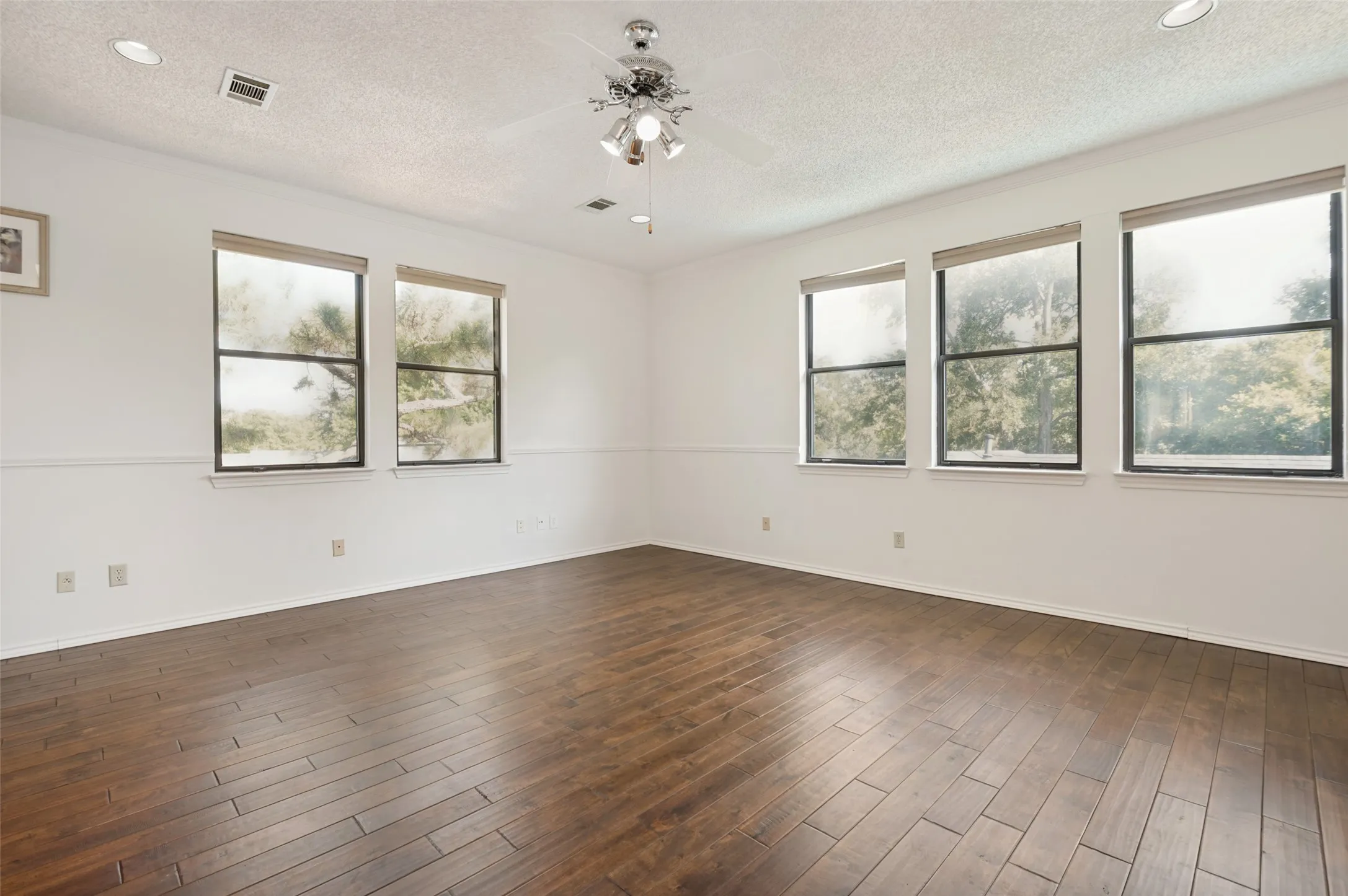 Spacious room upstairs room featuring wood-finish flooring, multiple windows, a ceiling fan, and recessed lighting.