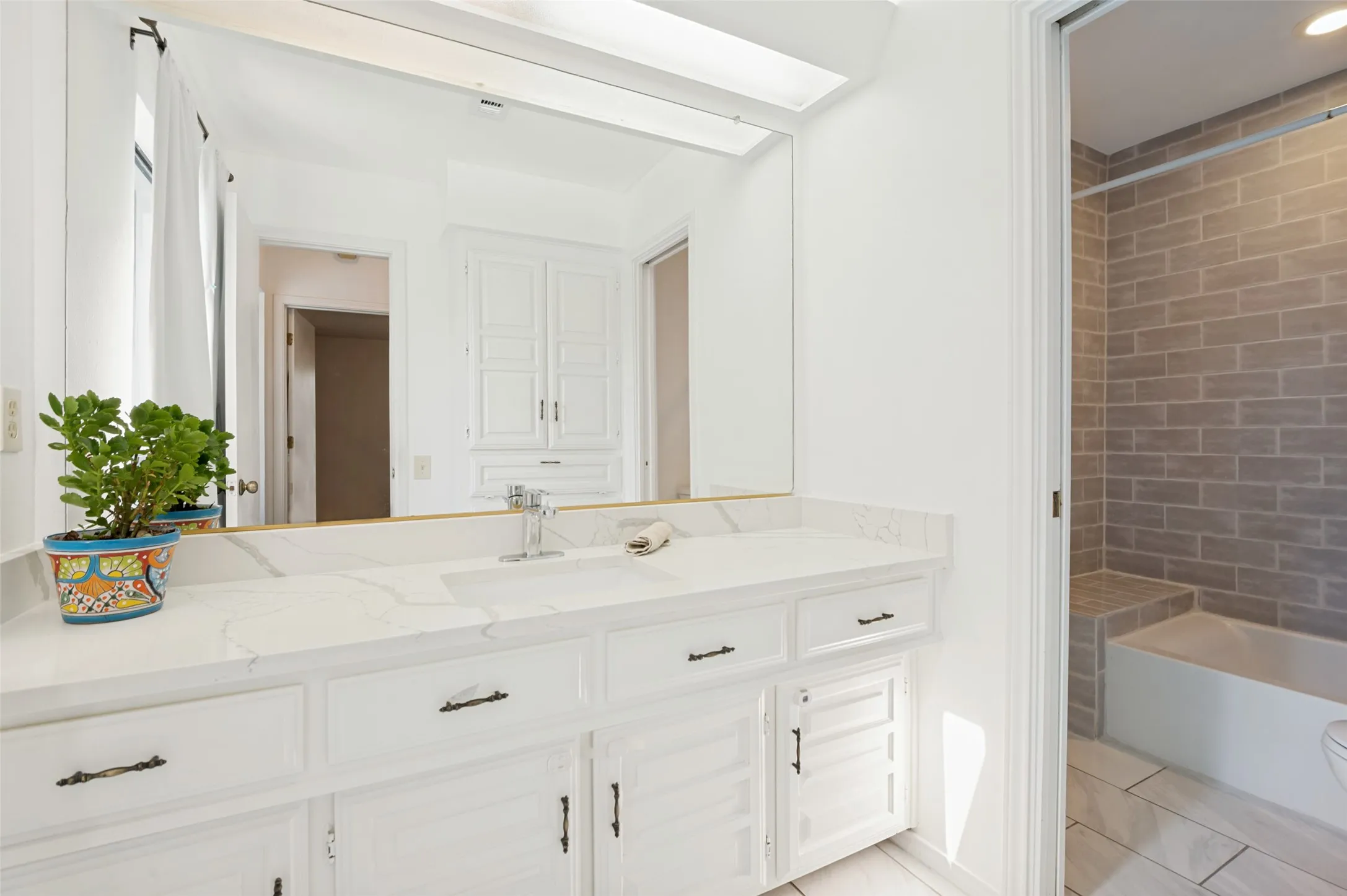 White vanity with integrated sink and chrome faucet, large rectangular mirror, and an adjacent shower/tub combination with subway tile surround and integrated bench