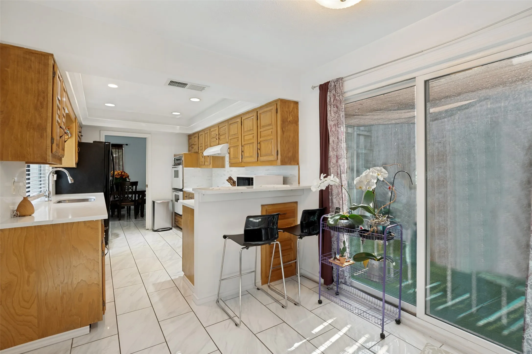 Kitchen featuring wood-finish cabinetry, white tile flooring, recessed lighting, and a sliding glass door