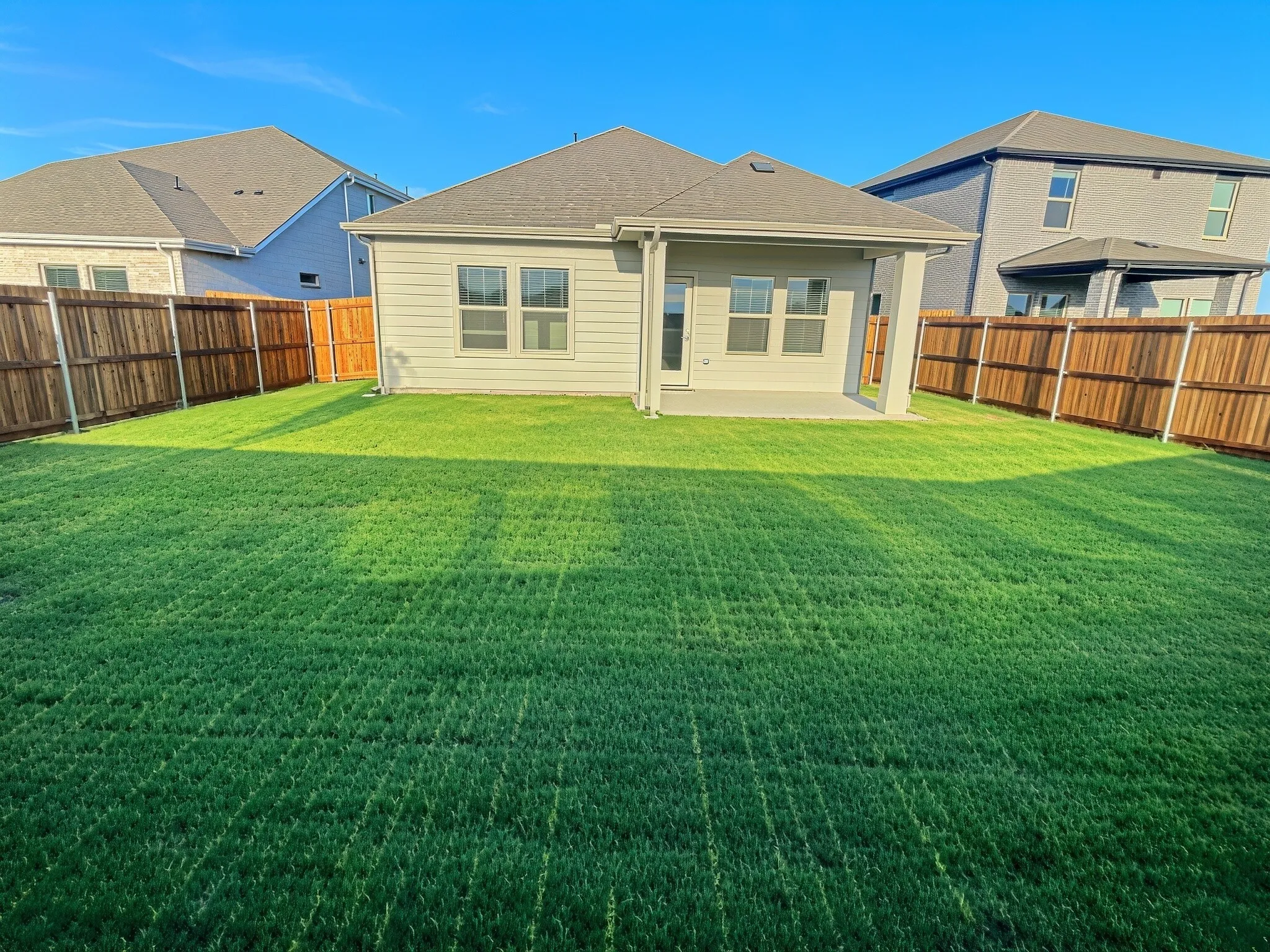 Expansive rear yard featuring green lawn, a covered patio, and wood privacy fencing