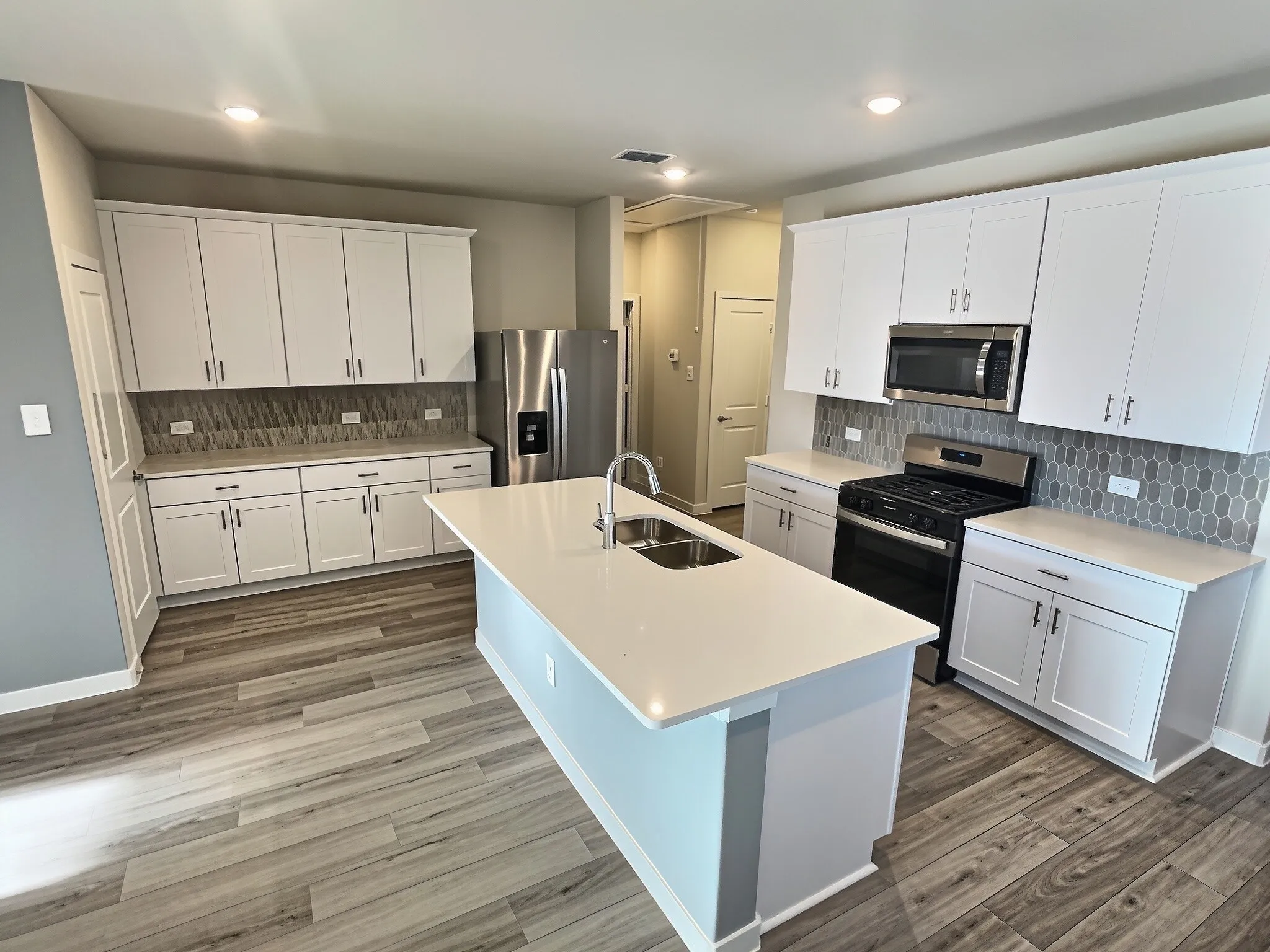 Kitchen featuring white cabinetry, light-toned countertops, a central island with an undermount sink, a stainless steel range, and wood-finish flooring