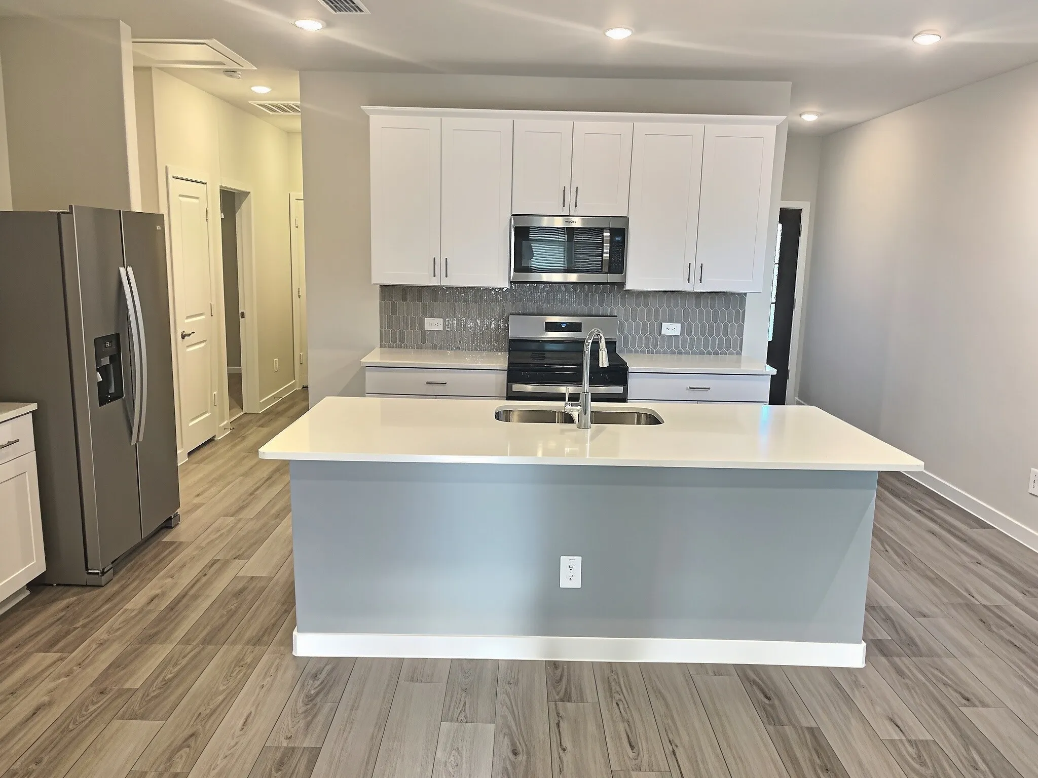 Kitchen featuring a center island with sink, stainless steel appliances, white cabinetry, and wood-finish flooring