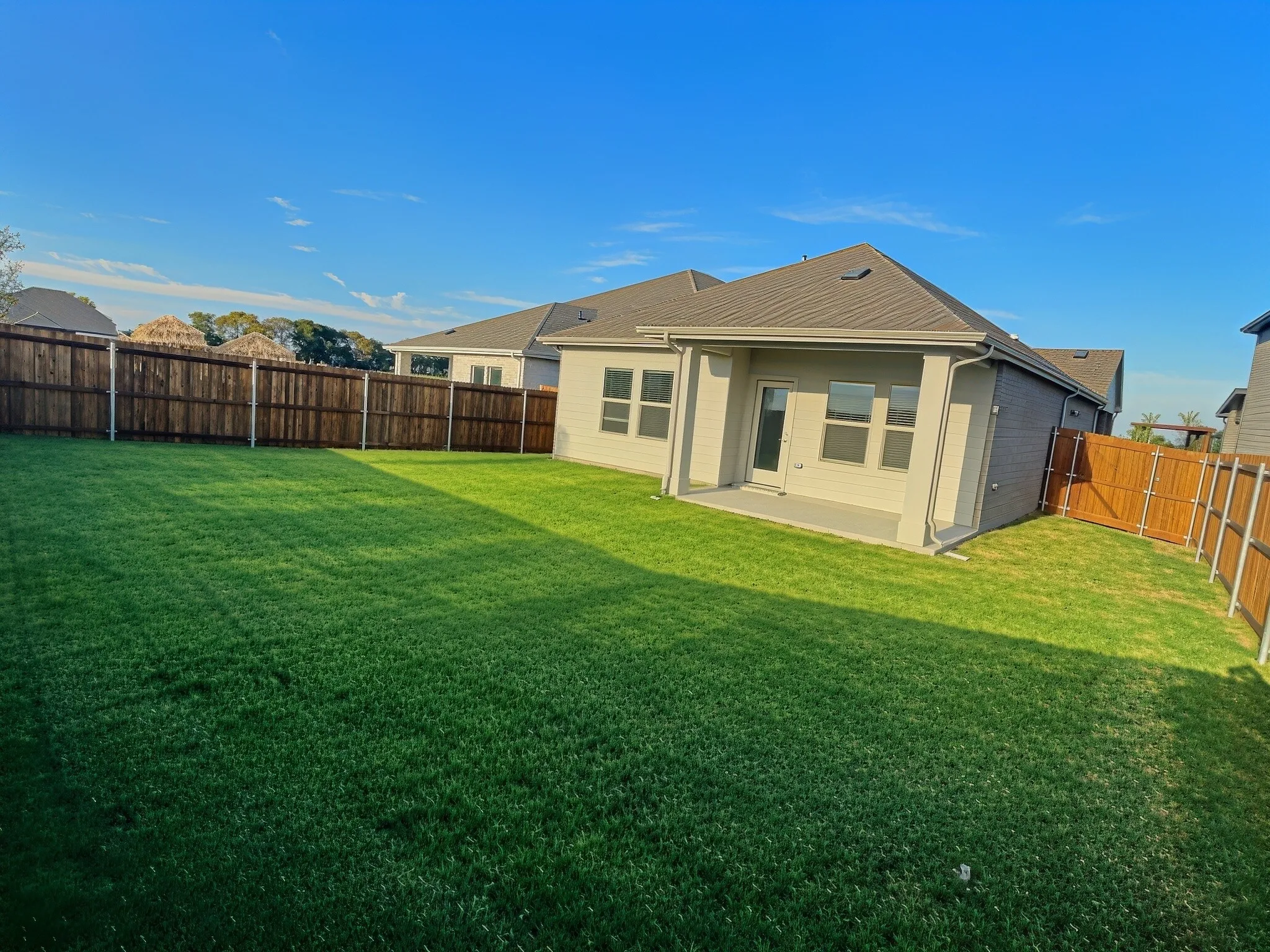 Expansive backyard featuring a manicured lawn, full privacy fencing, and a concrete patio