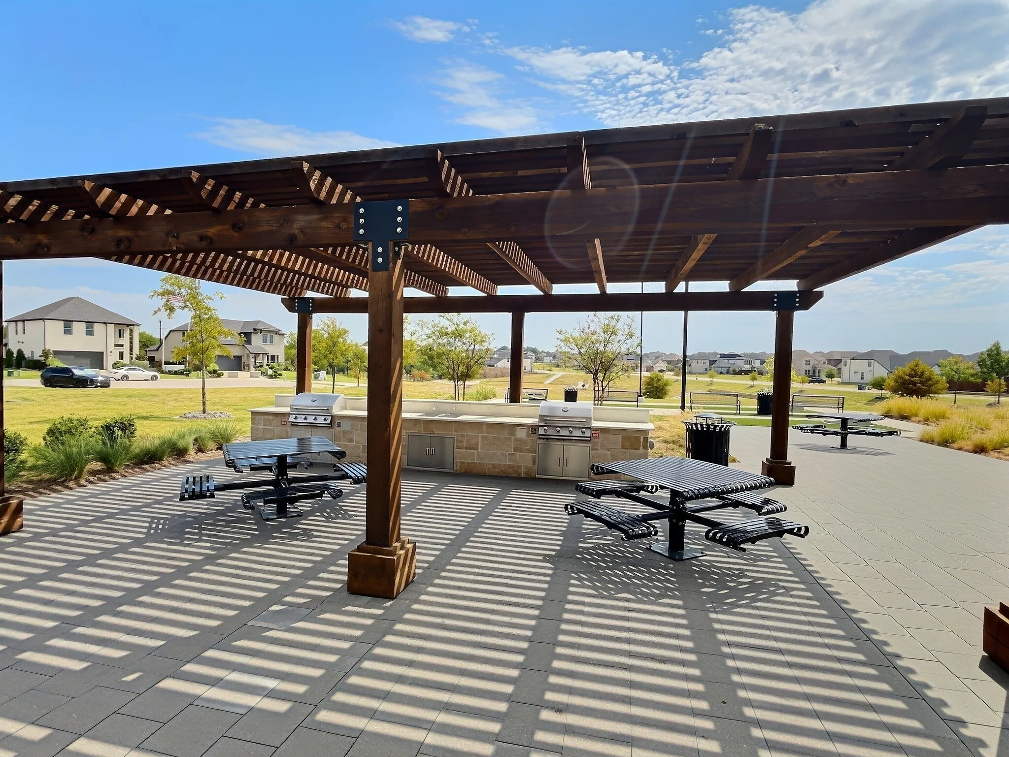 Wood pergola over a paved patio, featuring built-in grills, stone-finish counters, and mature landscaping