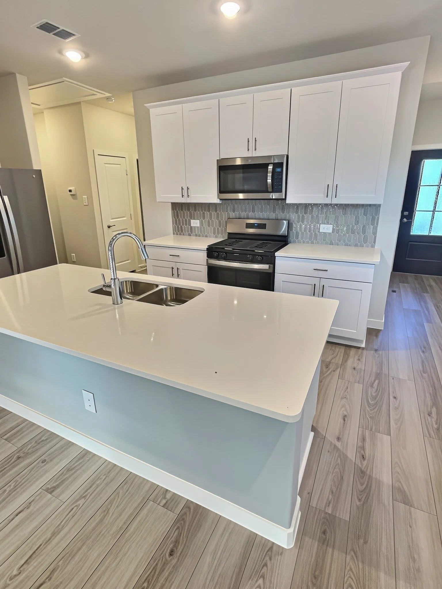 Modern kitchen featuring white shaker cabinetry, stainless steel appliances, a tile backsplash, light-toned countertops, and wood-finish flooring