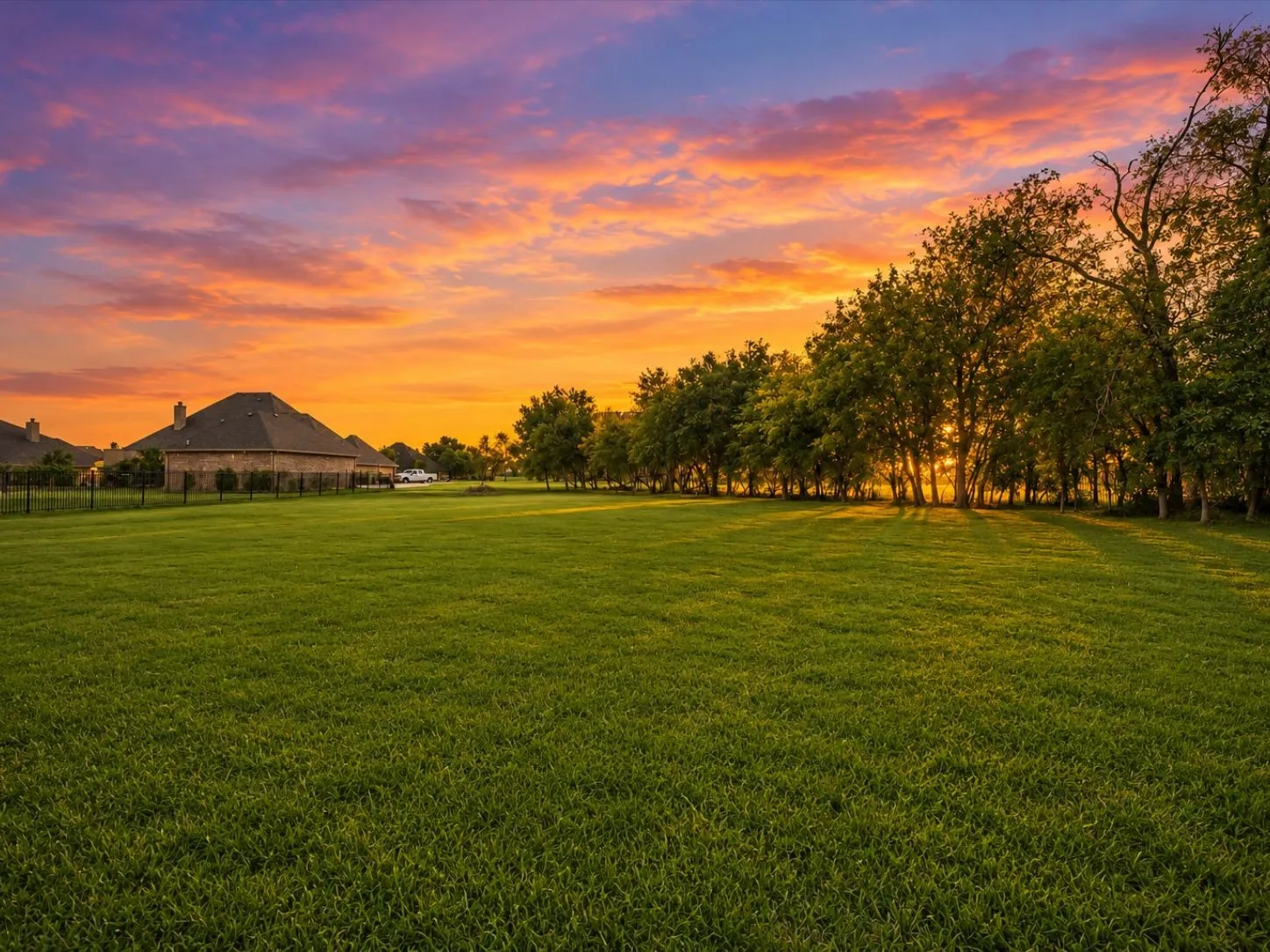 Expansive grassy lawn with surrounding mature trees and a brick-clad residence