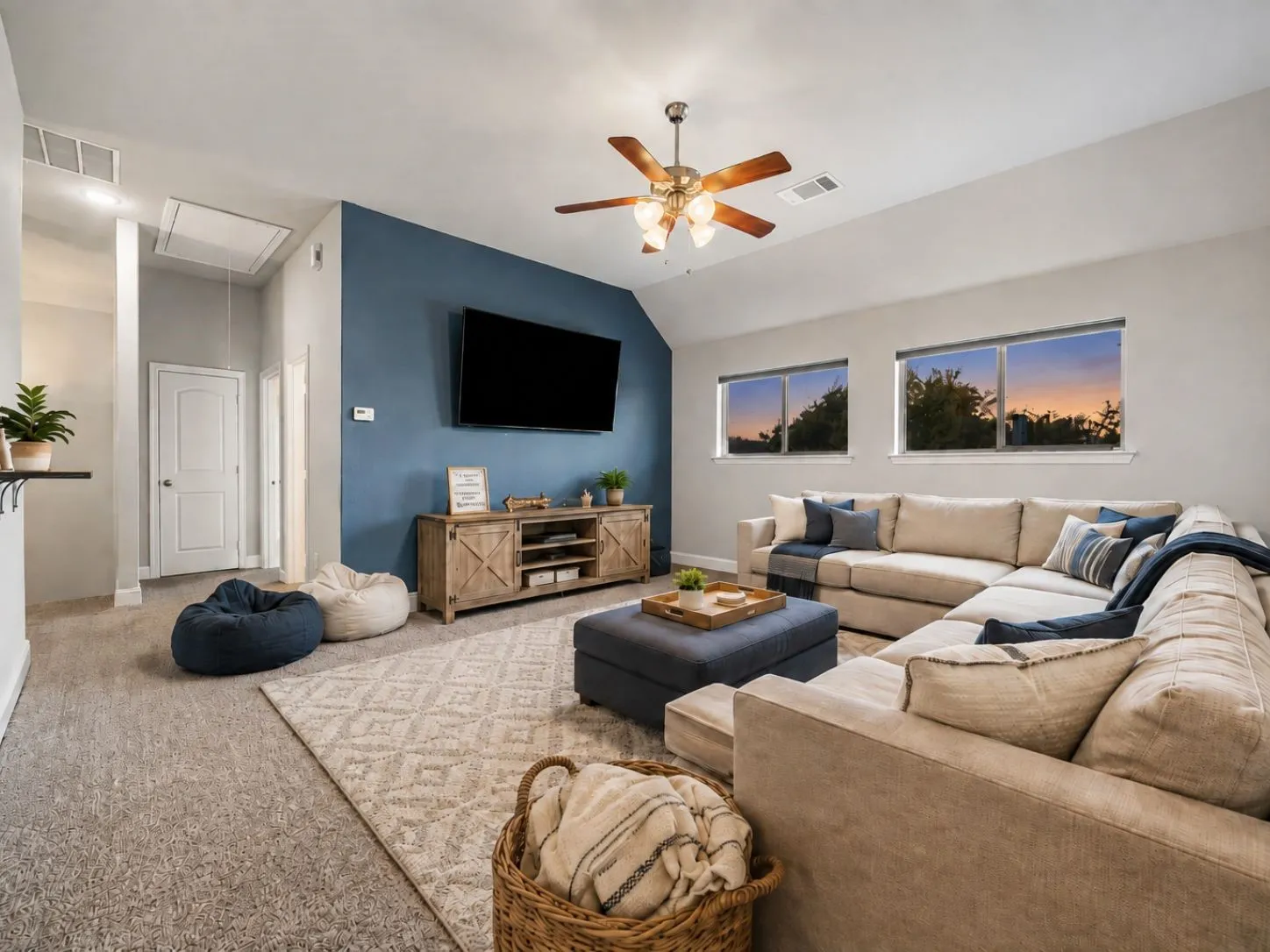 Vaulted ceiling with a ceiling fan, wall-mounted television, wood-finish media console, and two horizontal windows