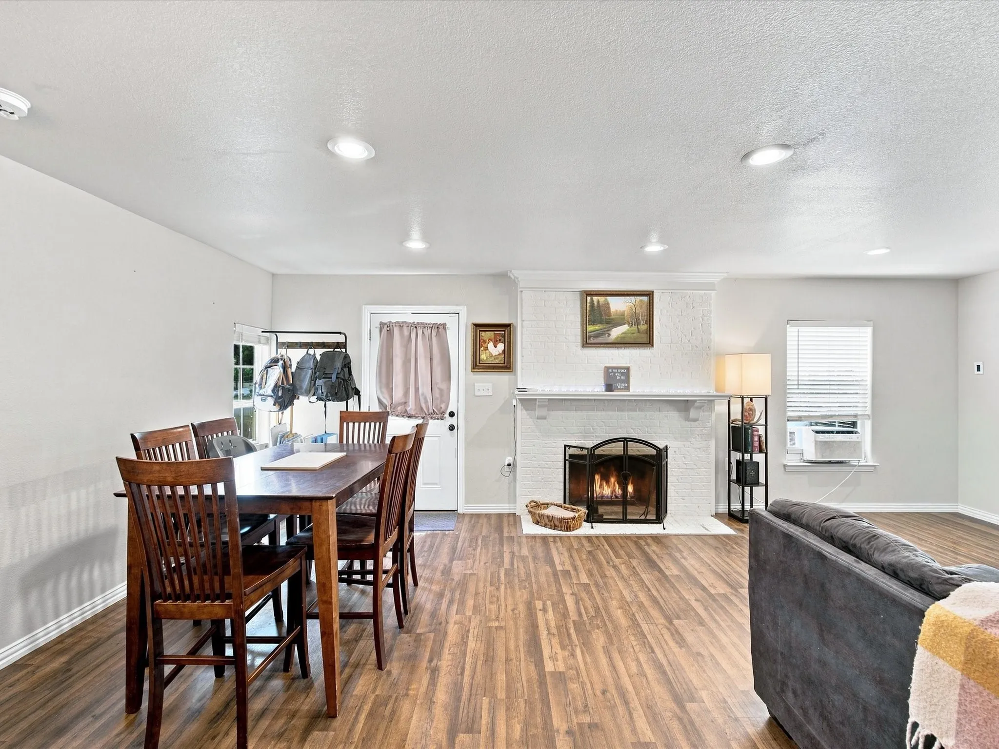 Wood-finish flooring, recessed lighting, white brick fireplace with mantel, white interior door, and window with blinds