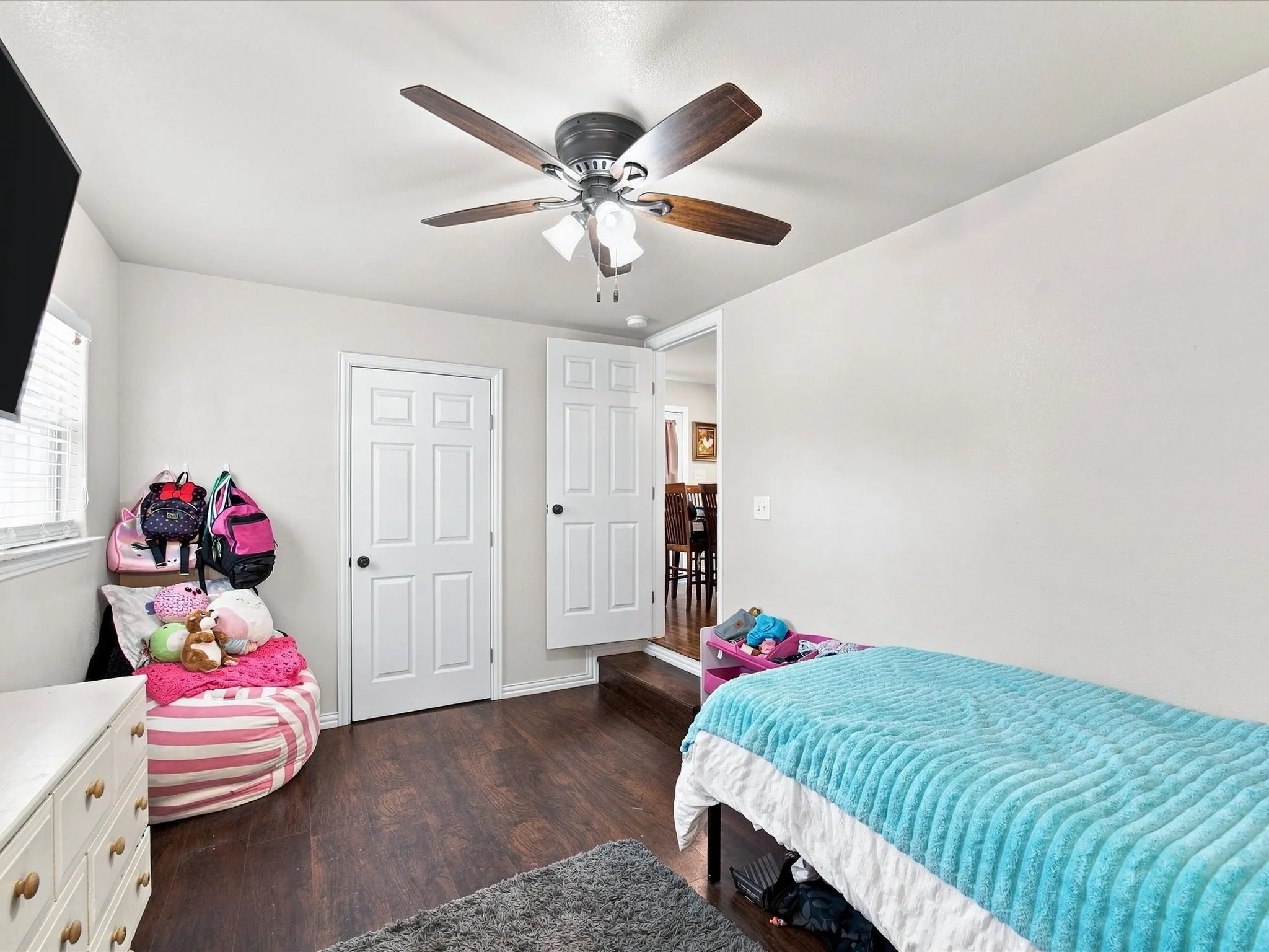 Recessed window with blinds, wood-finish flooring, two panel doors, and a ceiling fan with light fixture