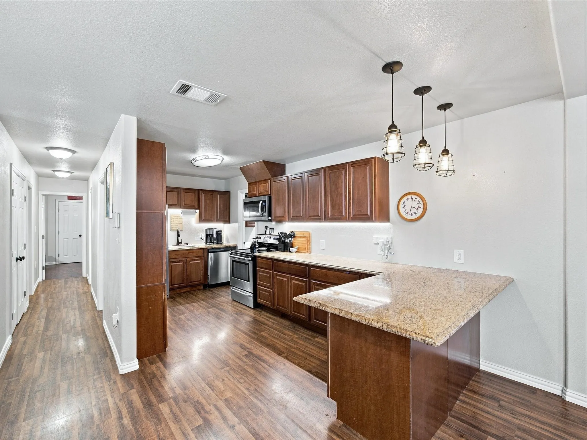 Kitchen featuring wood-finish flooring, dark wood cabinetry, stainless steel appliances, and a peninsula with a light-toned countertop