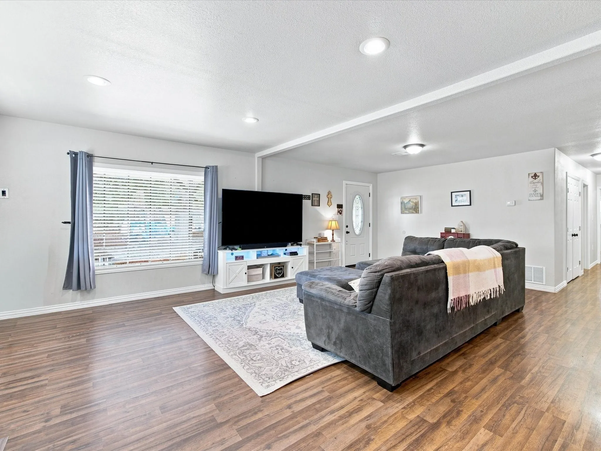 Wood-finish flooring throughout, recessed ceiling lighting, a white paneled door, and a single window with blinds