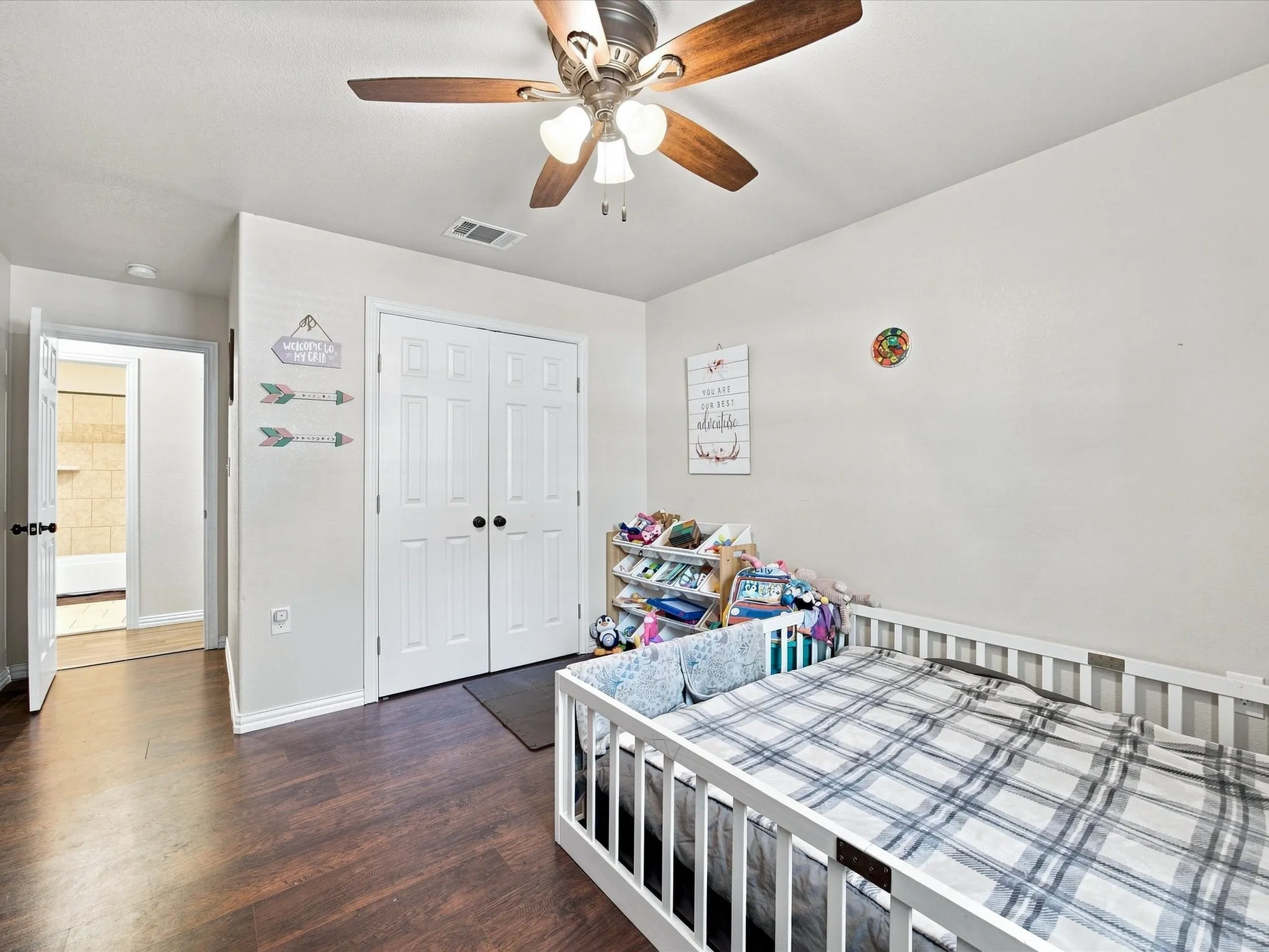 Wood-finish flooring, ceiling fan with integrated lighting, white paneled bifold closet doors, and a white interior door with dark hardware