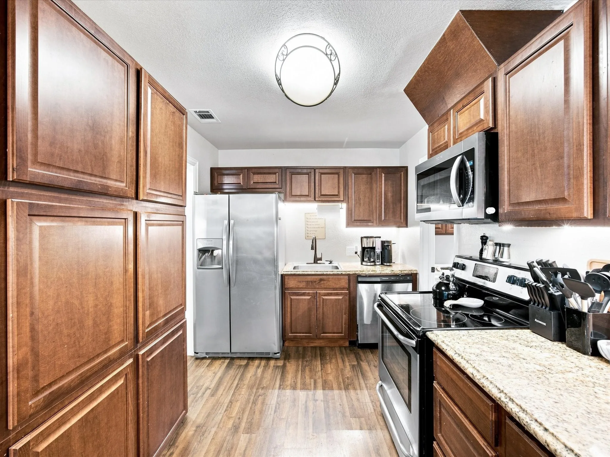 Kitchen featuring wood-finish cabinetry, stainless steel appliances, granite-style countertops, and wood-finish flooring