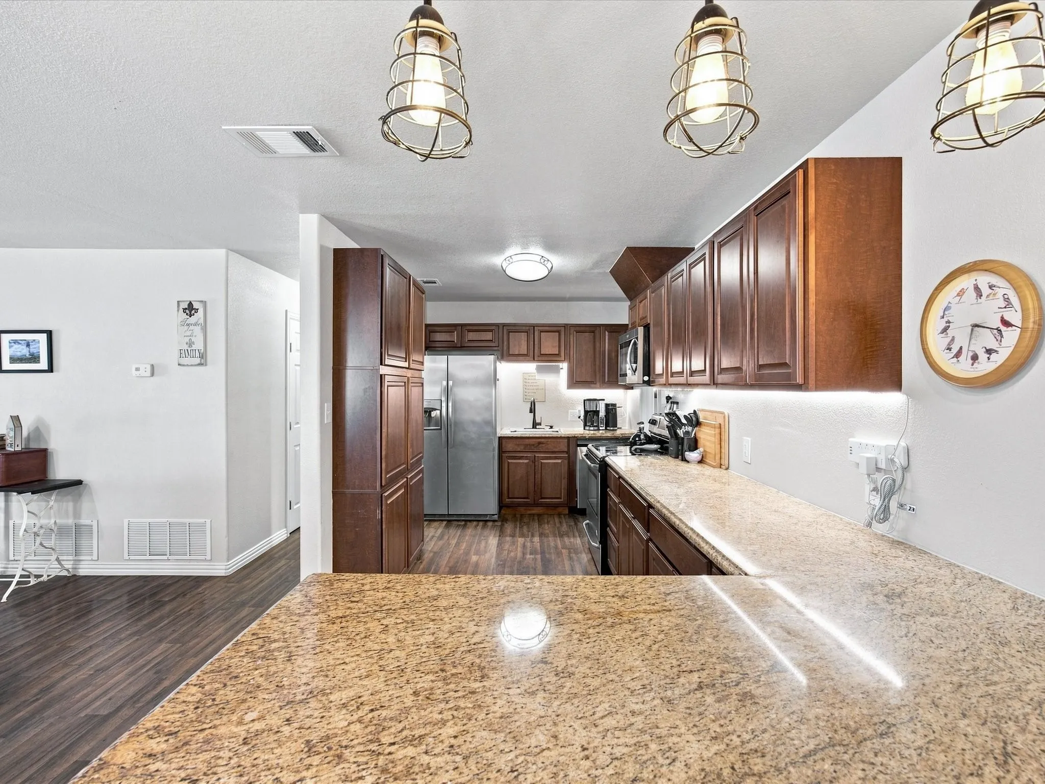 Kitchen with wood-finish flooring, dark wood cabinetry, stainless steel appliances, and light-toned countertops