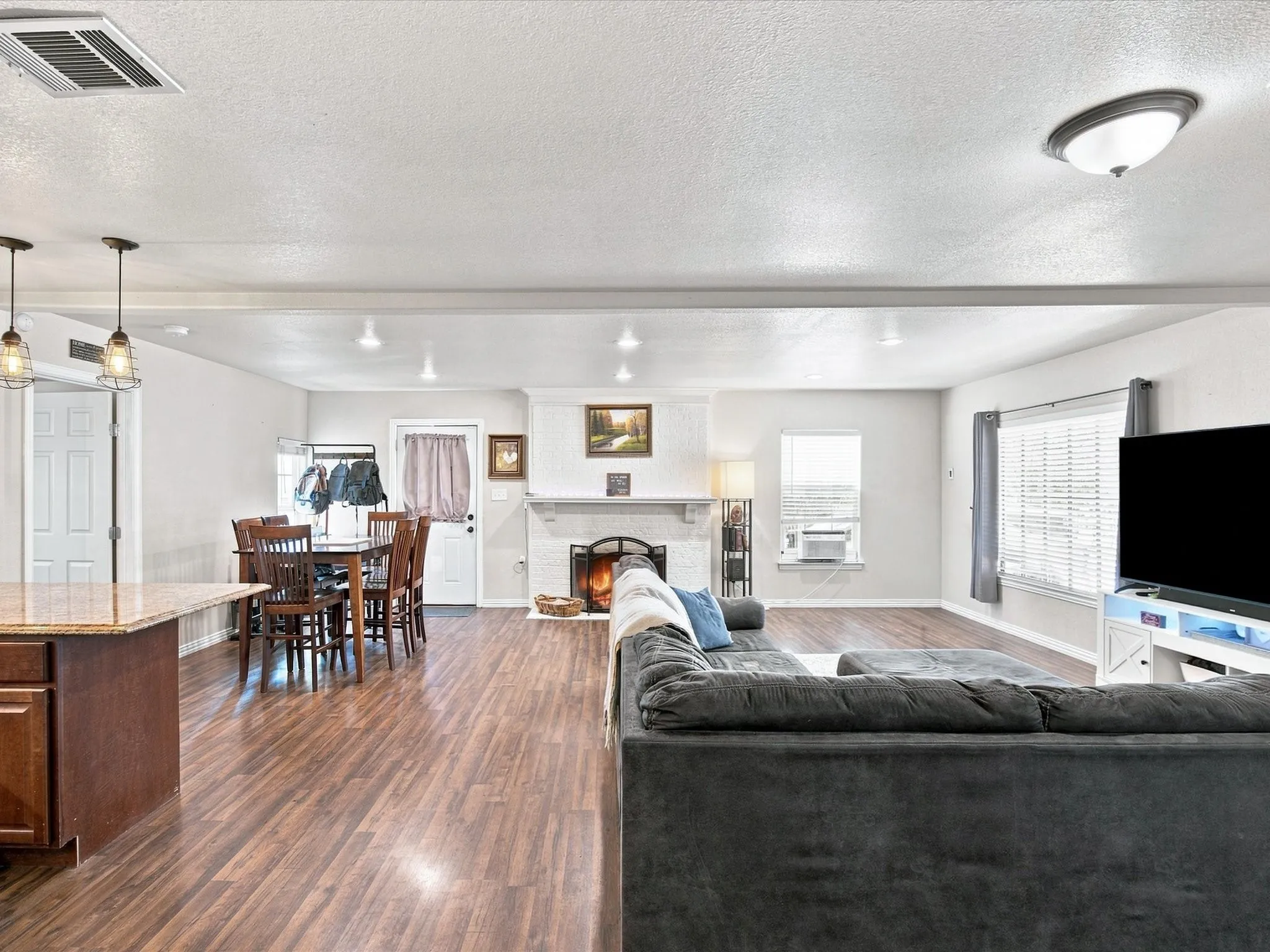 Open-concept living space with wood-finish flooring, recessed lighting, and a white brick fireplace