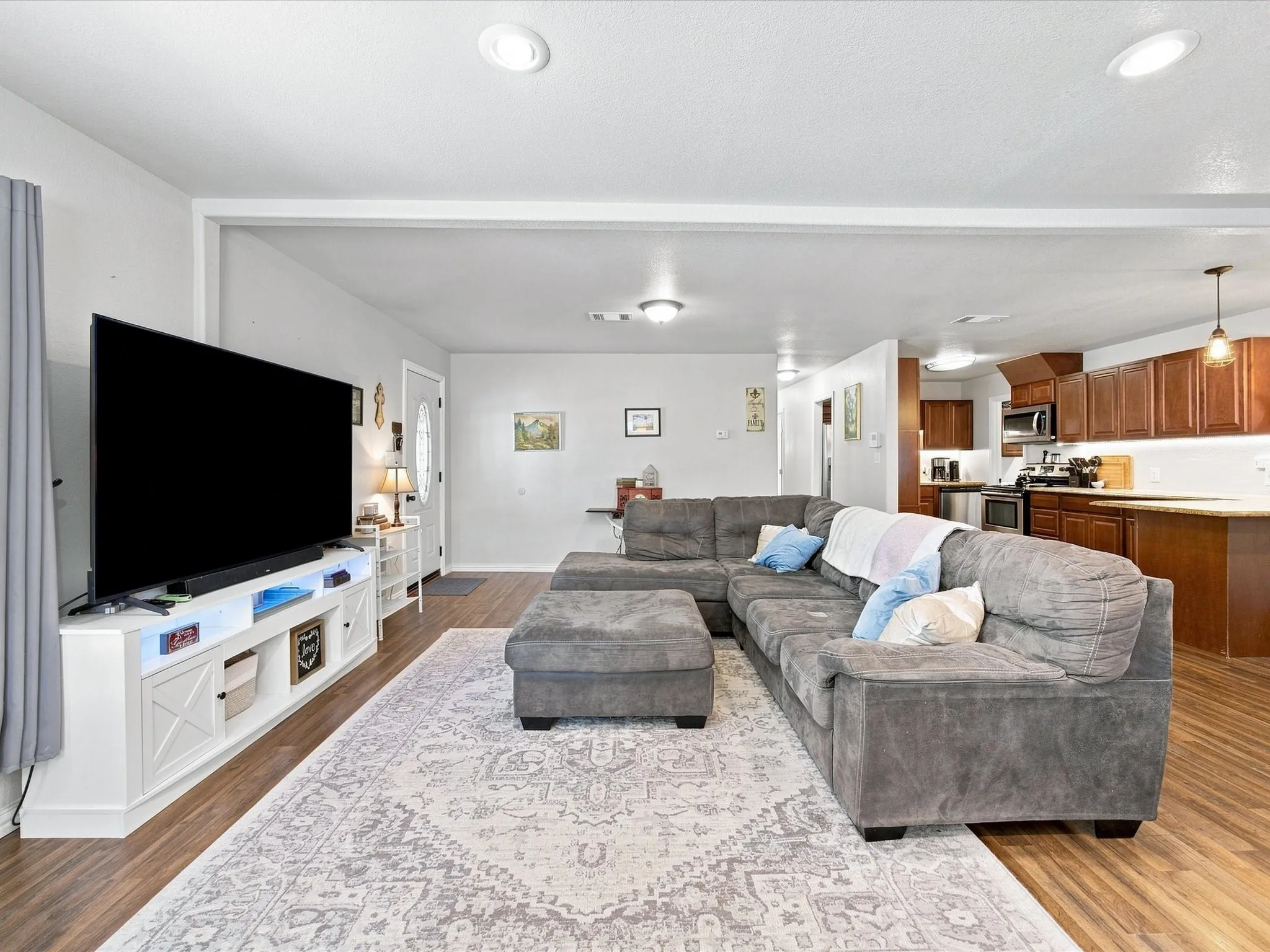 Recessed ceiling lighting, wood-finish flooring, kitchen with wood cabinetry, stainless steel appliances, and light-toned countertops