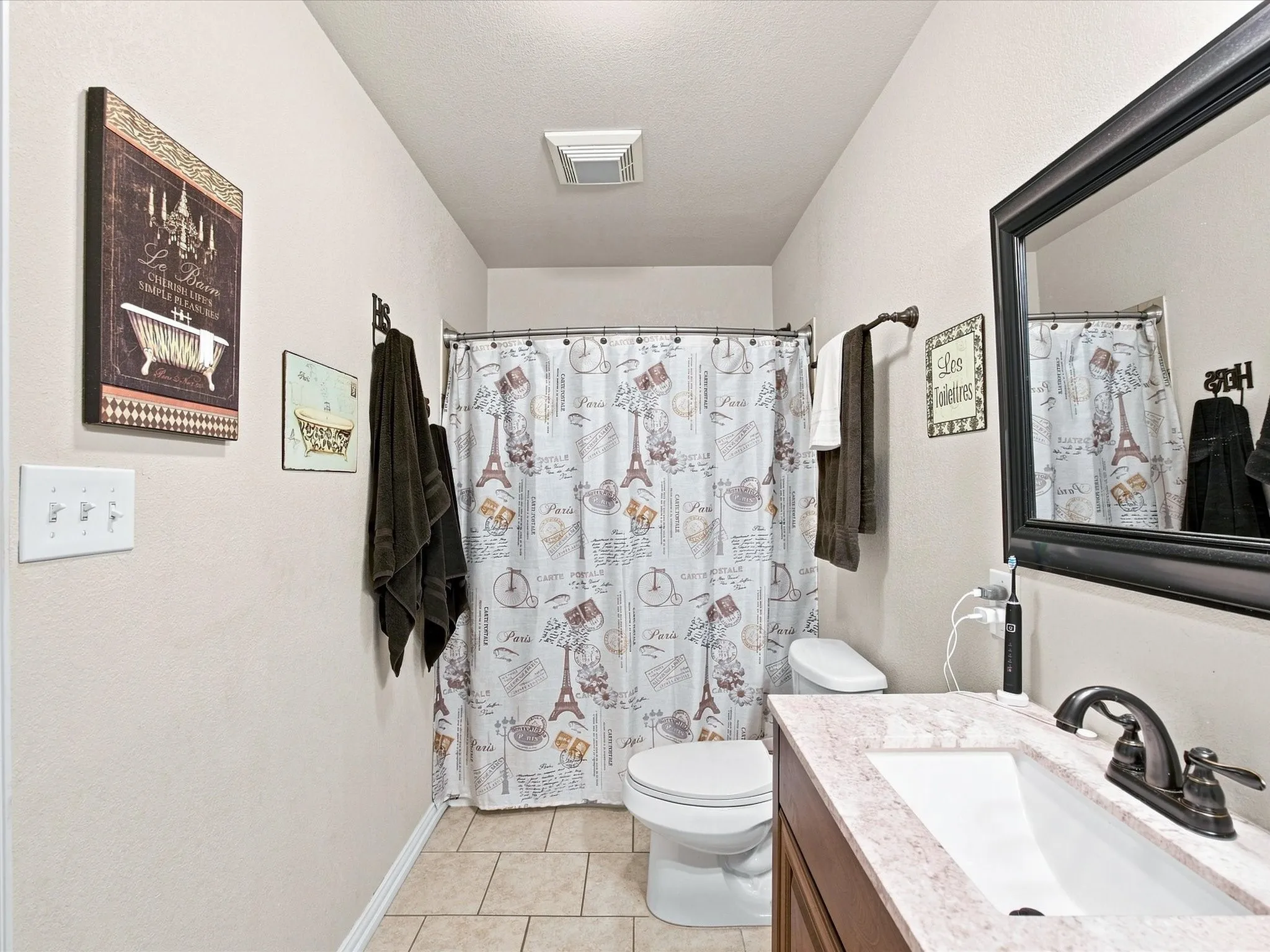 Tile flooring, vanity with integrated sink, dark wood-finish cabinetry, framed wall mirror, and a shower/tub combination