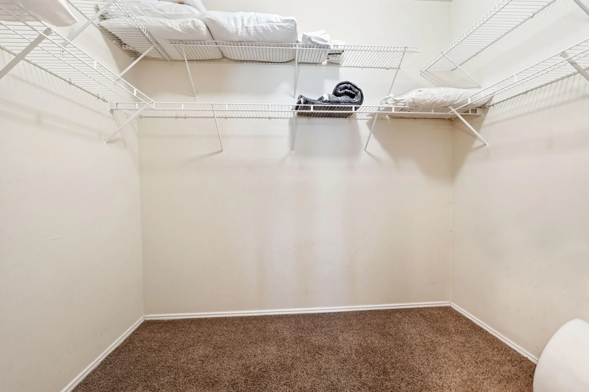 Spacious closet featuring neutral walls, carpeted flooring, and wire shelving system with multiple storage levels and hanging capacity