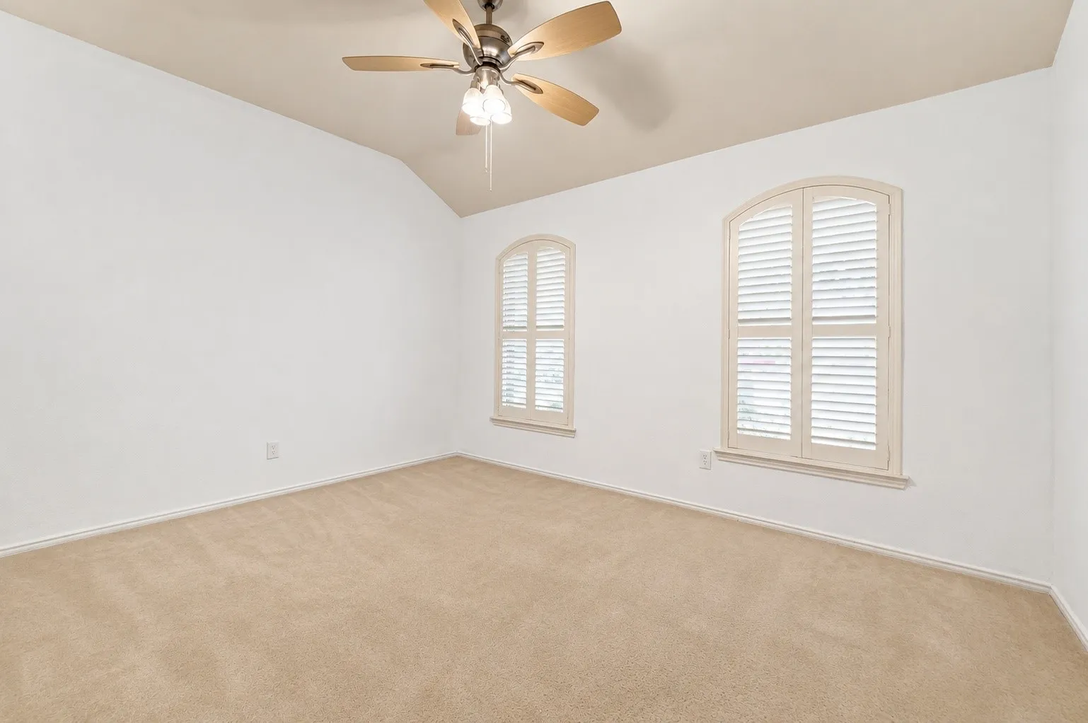 Sloped ceiling with an attached ceiling fan, two arched windows with louvered shutters, and wall-to-wall carpeting
