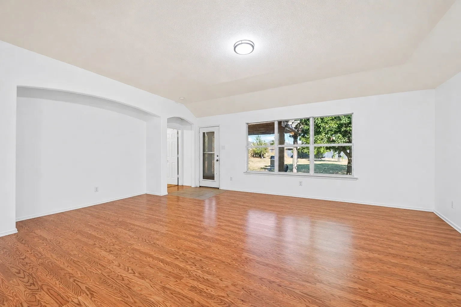 Spacious living area featuring wood-finish flooring, a large multi-pane window, and an arched entry