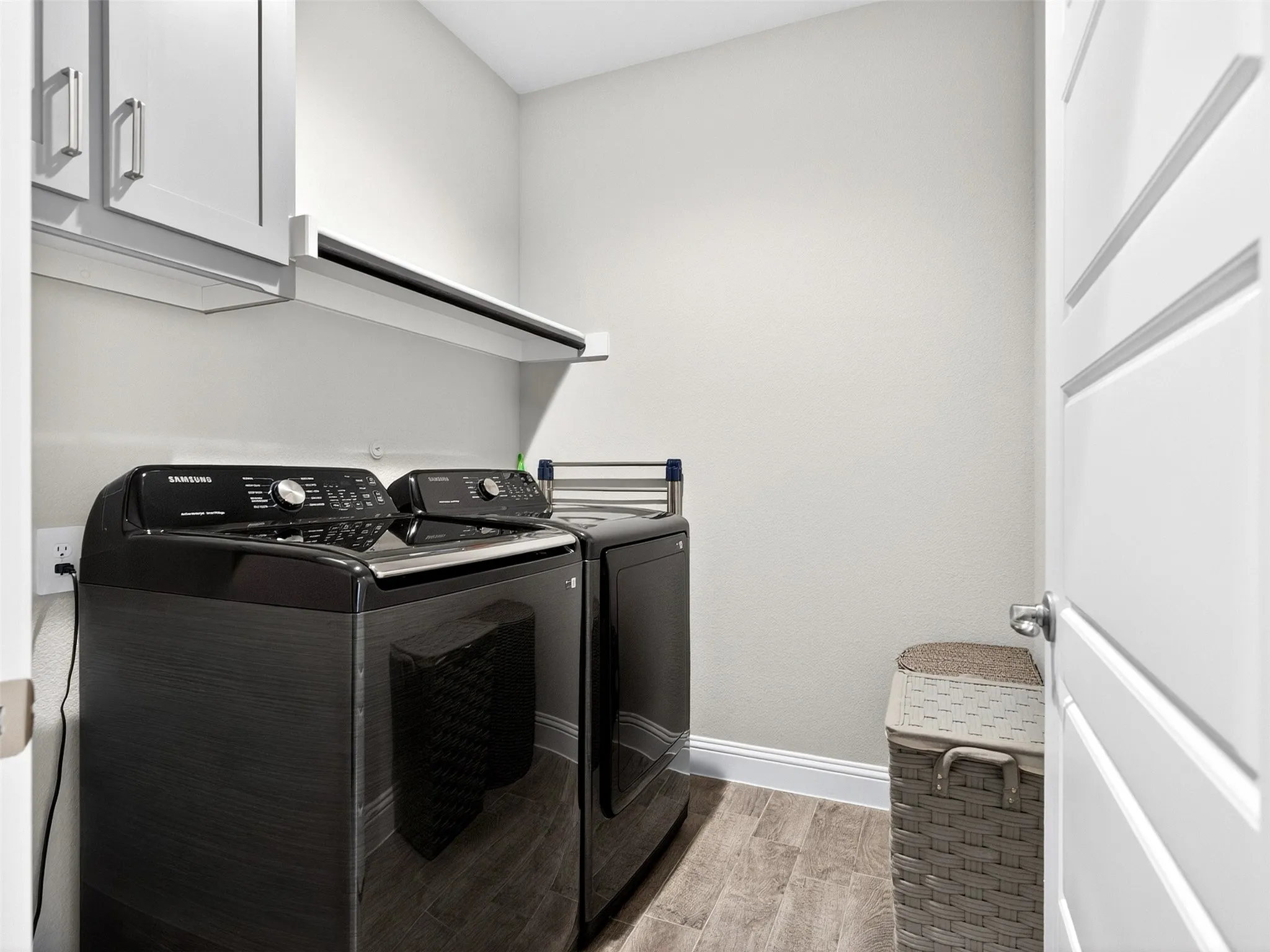 Laundry area featuring wood-finish flooring, white cabinetry with brushed nickel hardware, and a wall-mounted shelving unit