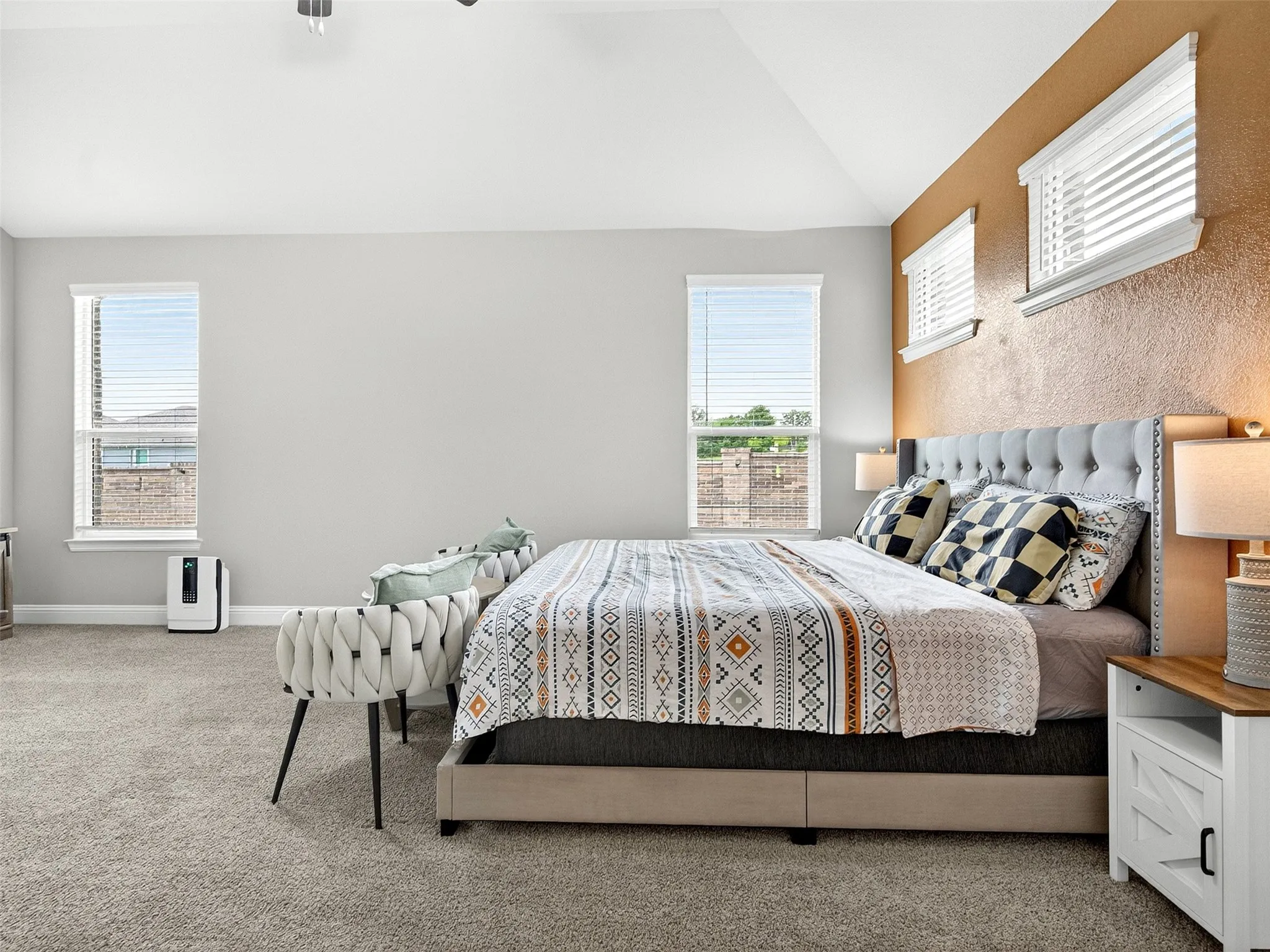 Vaulted ceiling, textured accent wall, light-colored carpet, multiple windows, and a built-in ceiling light fixture