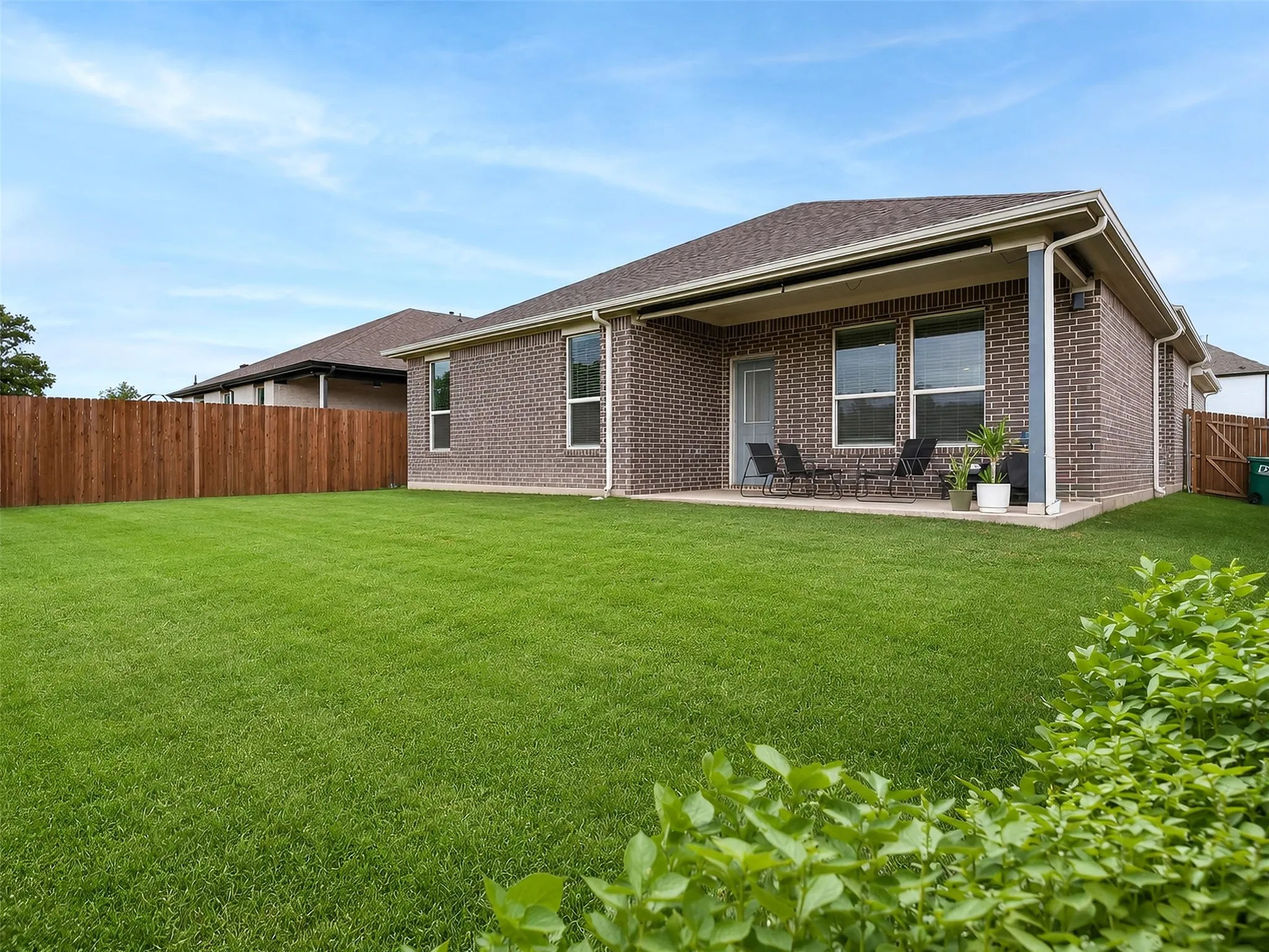 Expansive backyard with a manicured lawn, full privacy fencing, and a covered patio