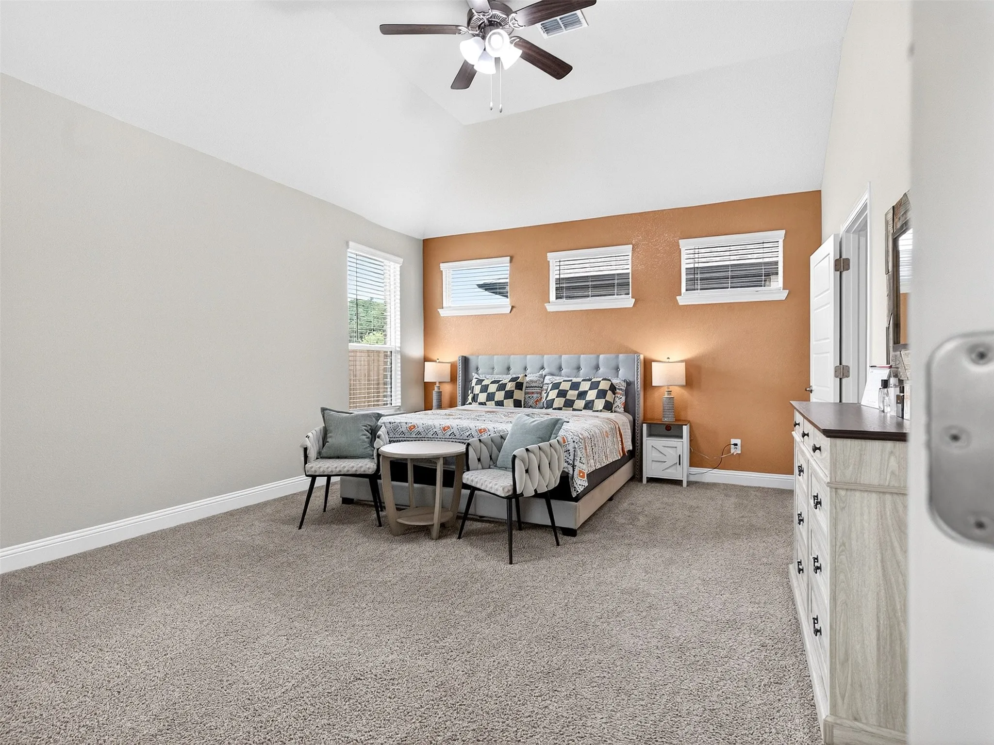 Vaulted ceiling, ceiling fan, carpet flooring, multiple windows, and a built-in dresser