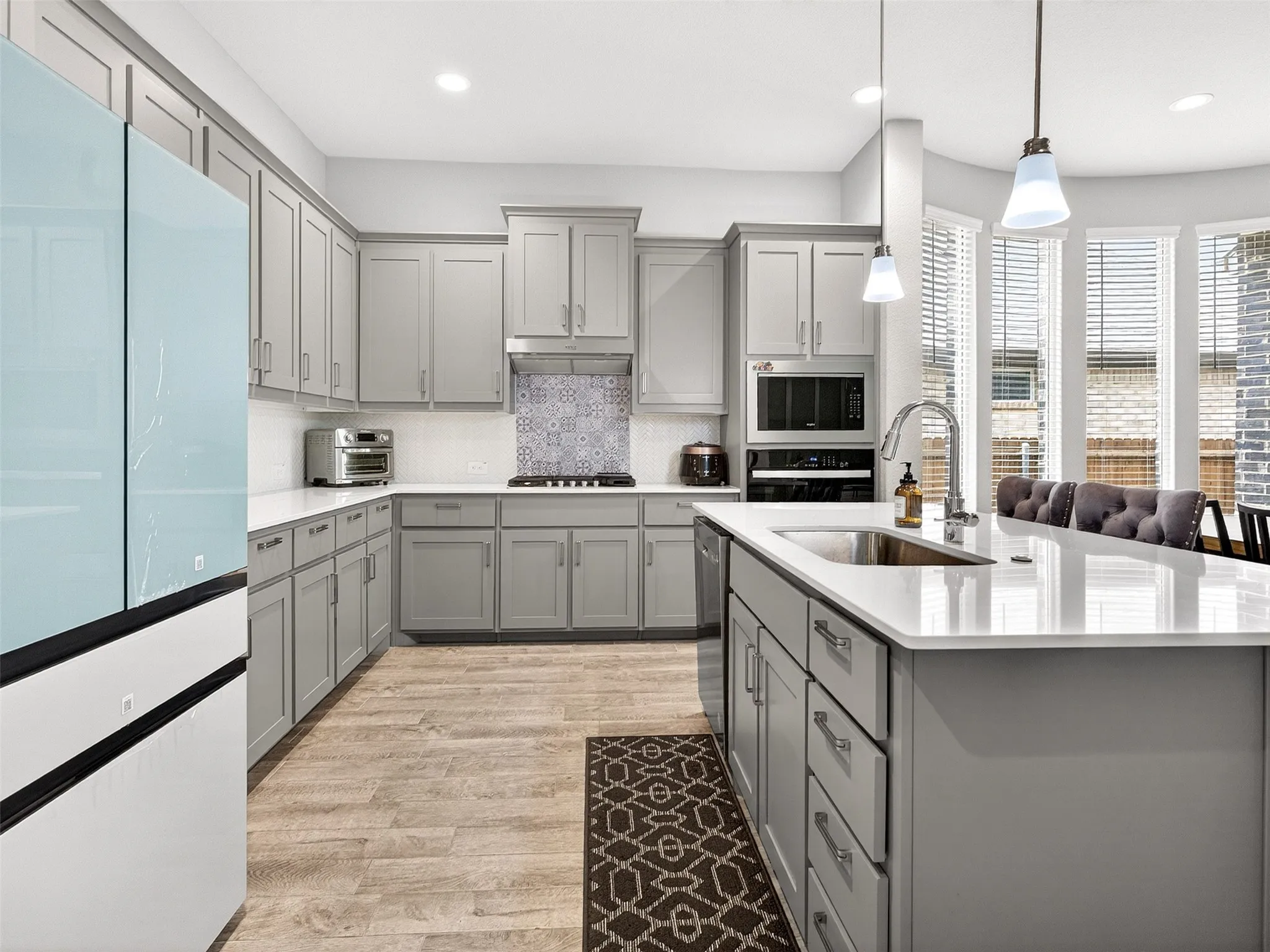 Kitchen featuring light gray cabinetry, white countertops, wood-finish flooring, a patterned tile backsplash, and a large center island with an integrated sink